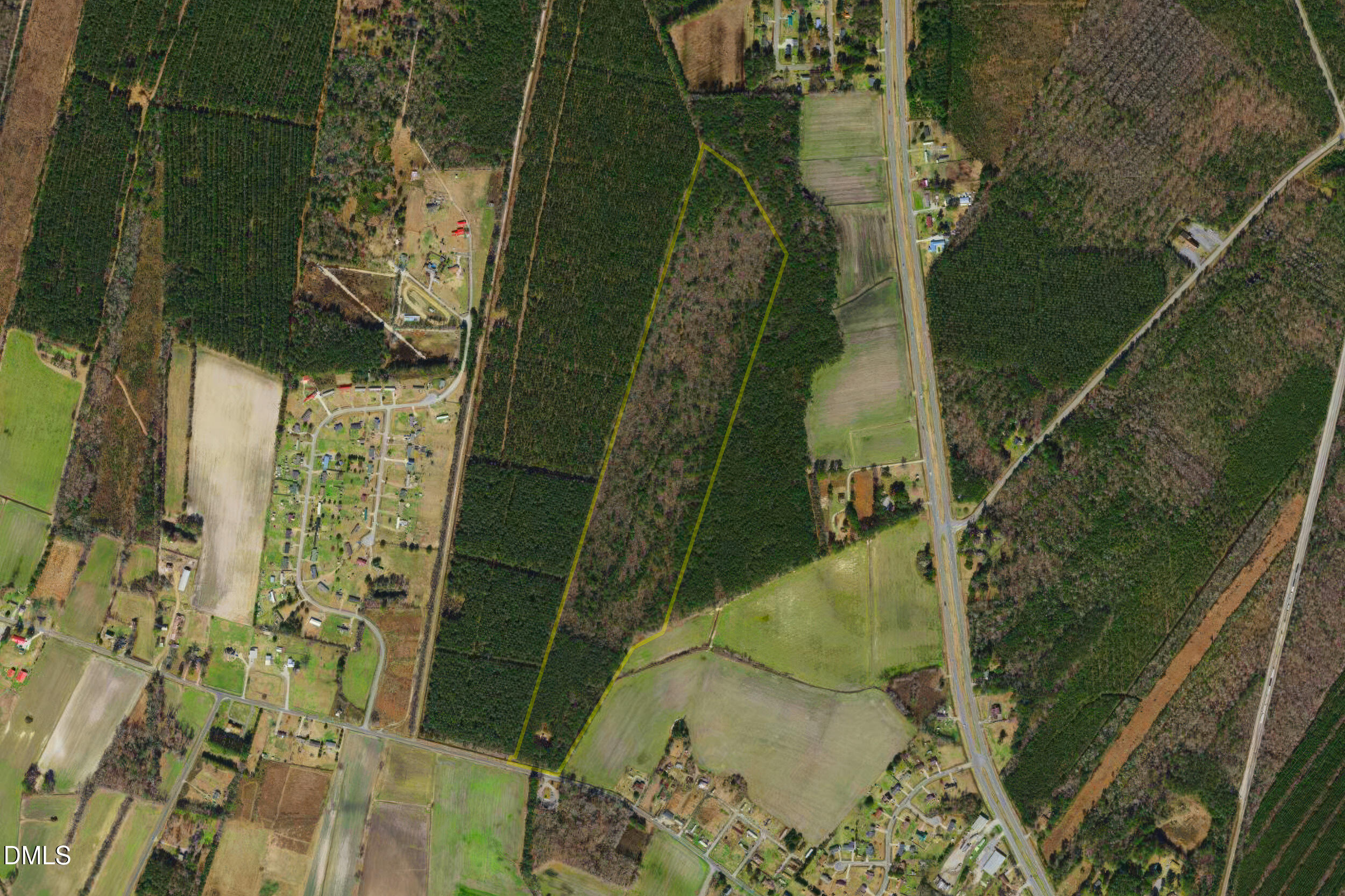 Aerial view of a wooded rural parcel outlined in yellow beside fields and scattered homes.