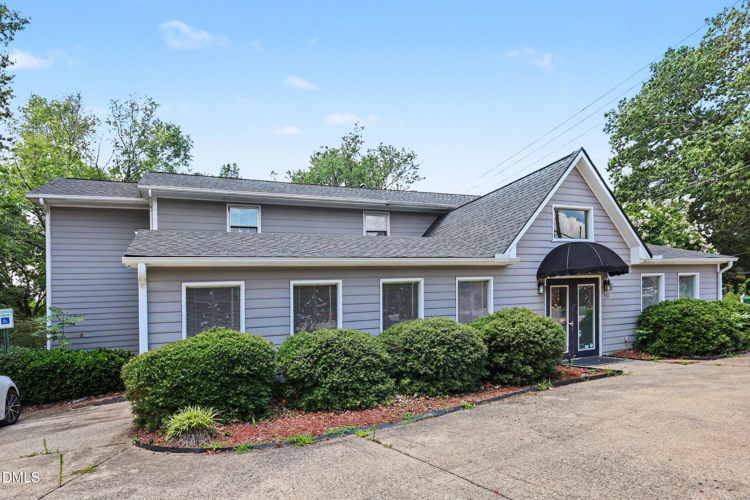 Gray two-story building with a steep front gable, black entrance awning, and trimmed shrubs.
