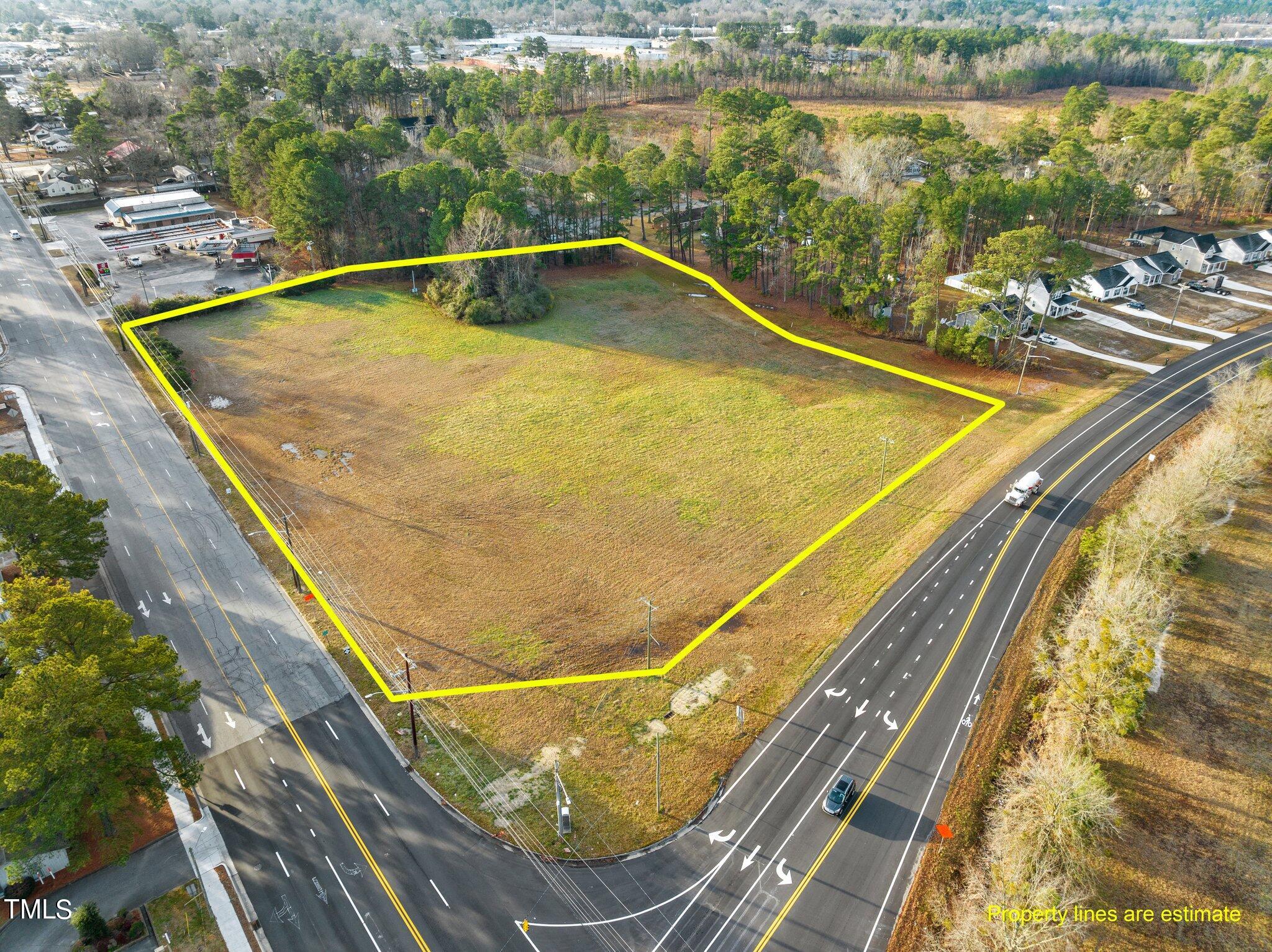 Aerial view of vacant land outlined in yellow between two roads, with homes and trees nearby.