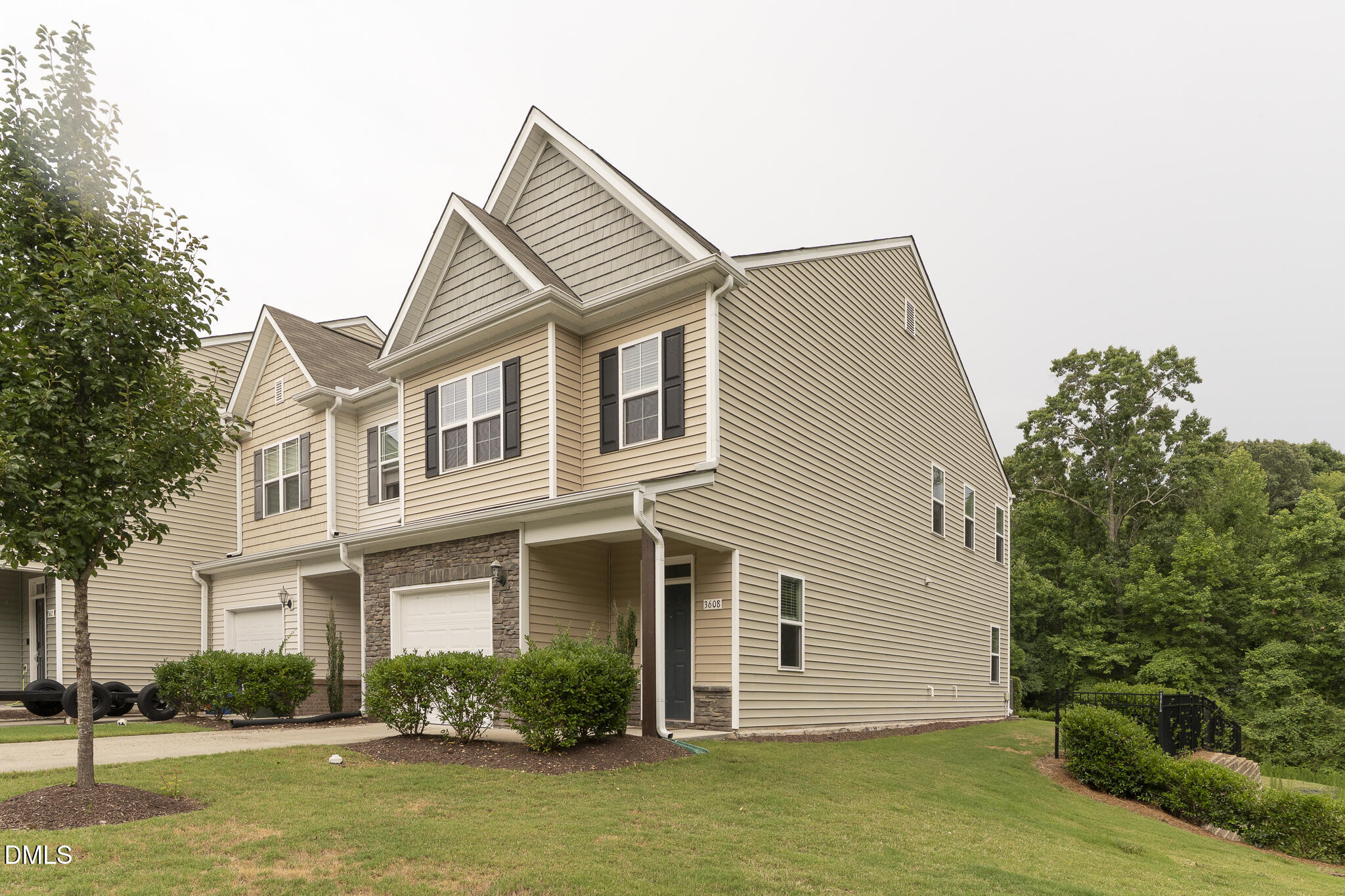 Beige townhouse with stone-accented garage, covered entry, and landscaped lawn.