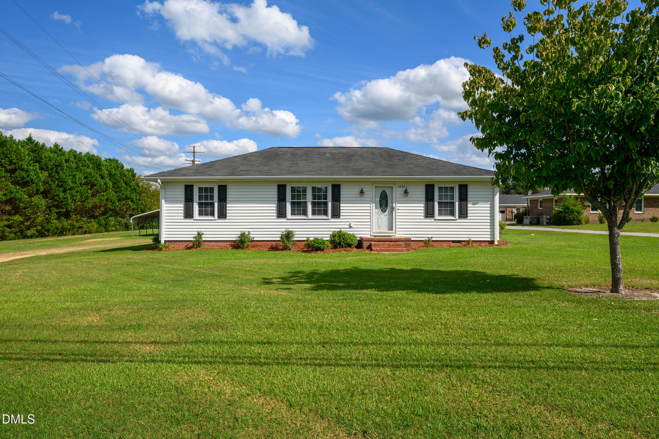 White single-story house with black shutters, brick steps, and a broad lawn.
