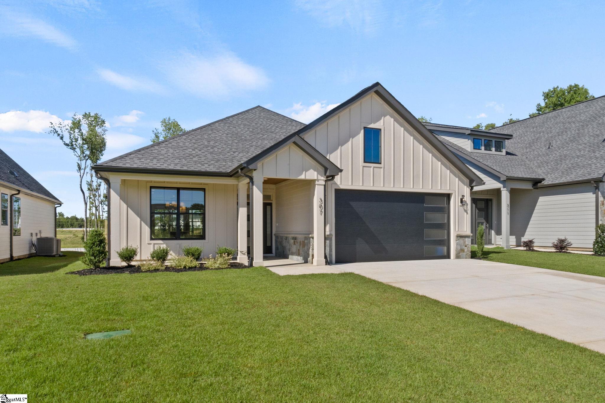 Modern light-sided home with a dark garage door, covered entry, and green lawn.