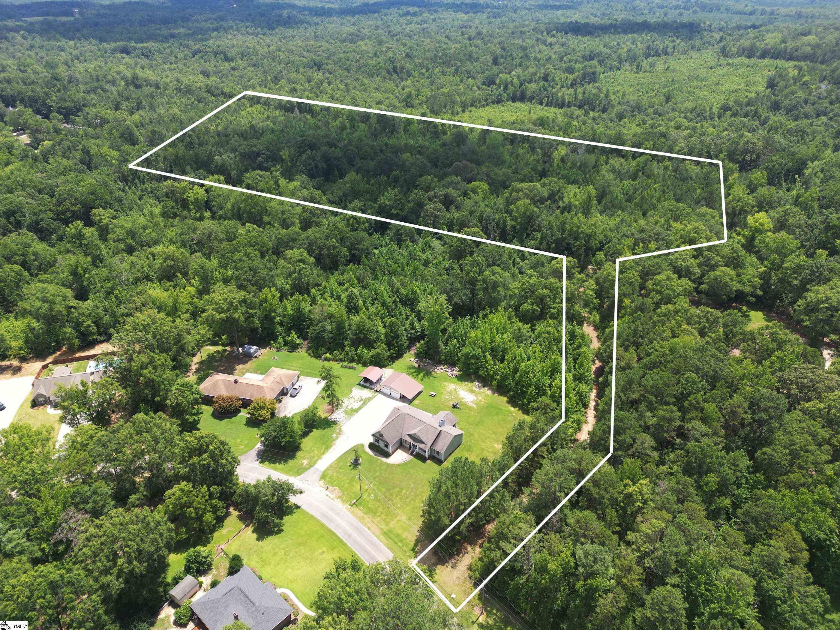 Aerial view of a large wooded parcel outlined in white, with homes and lawns along the road.