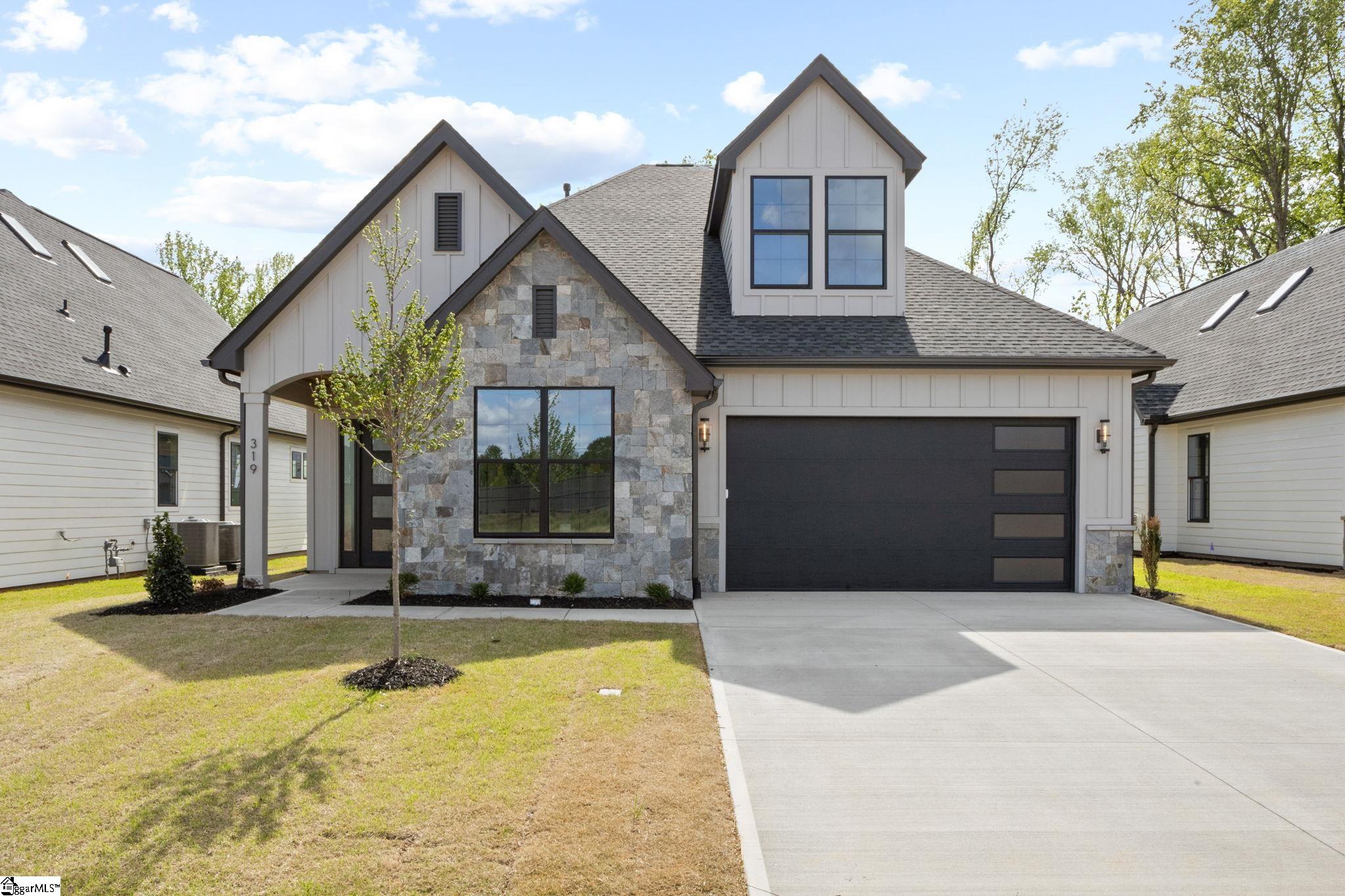 Modern two-story house with a gray stone facade, dark garage door, and wide driveway.
