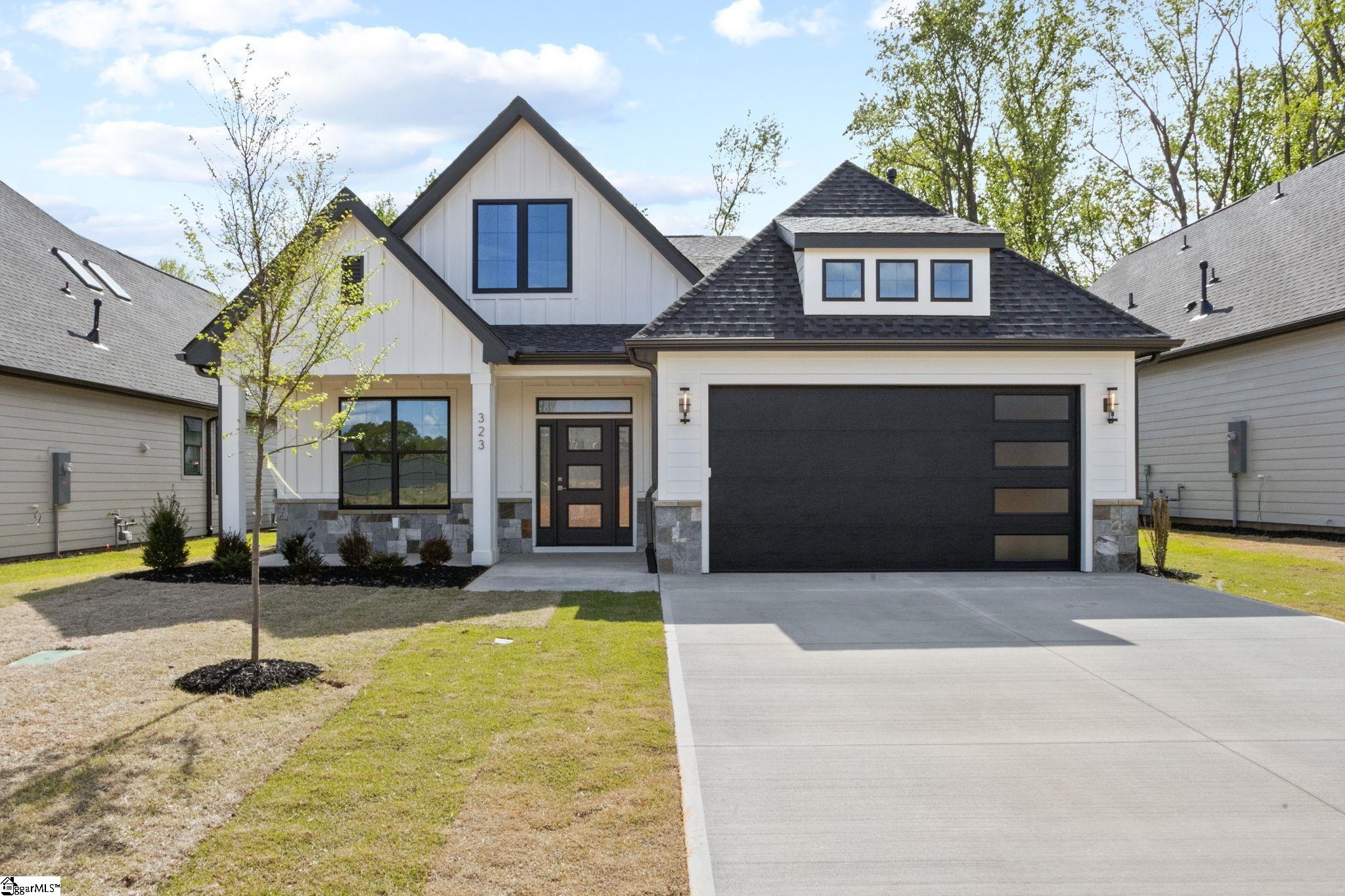Modern white gabled home with dark trim, stone accents, and a wide black garage door.