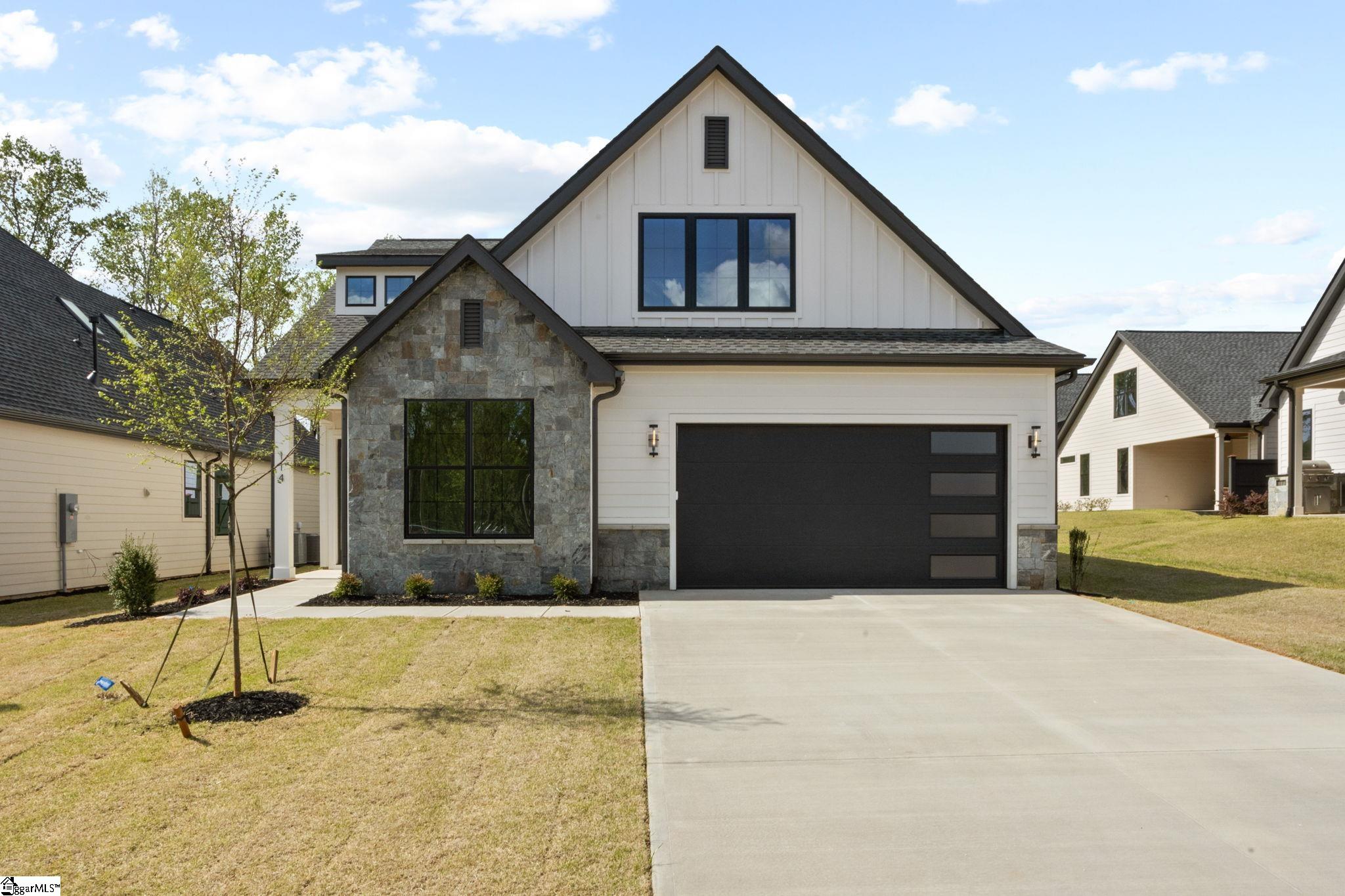 Two-story white house with a stone facade, black garage door, and wide concrete driveway.