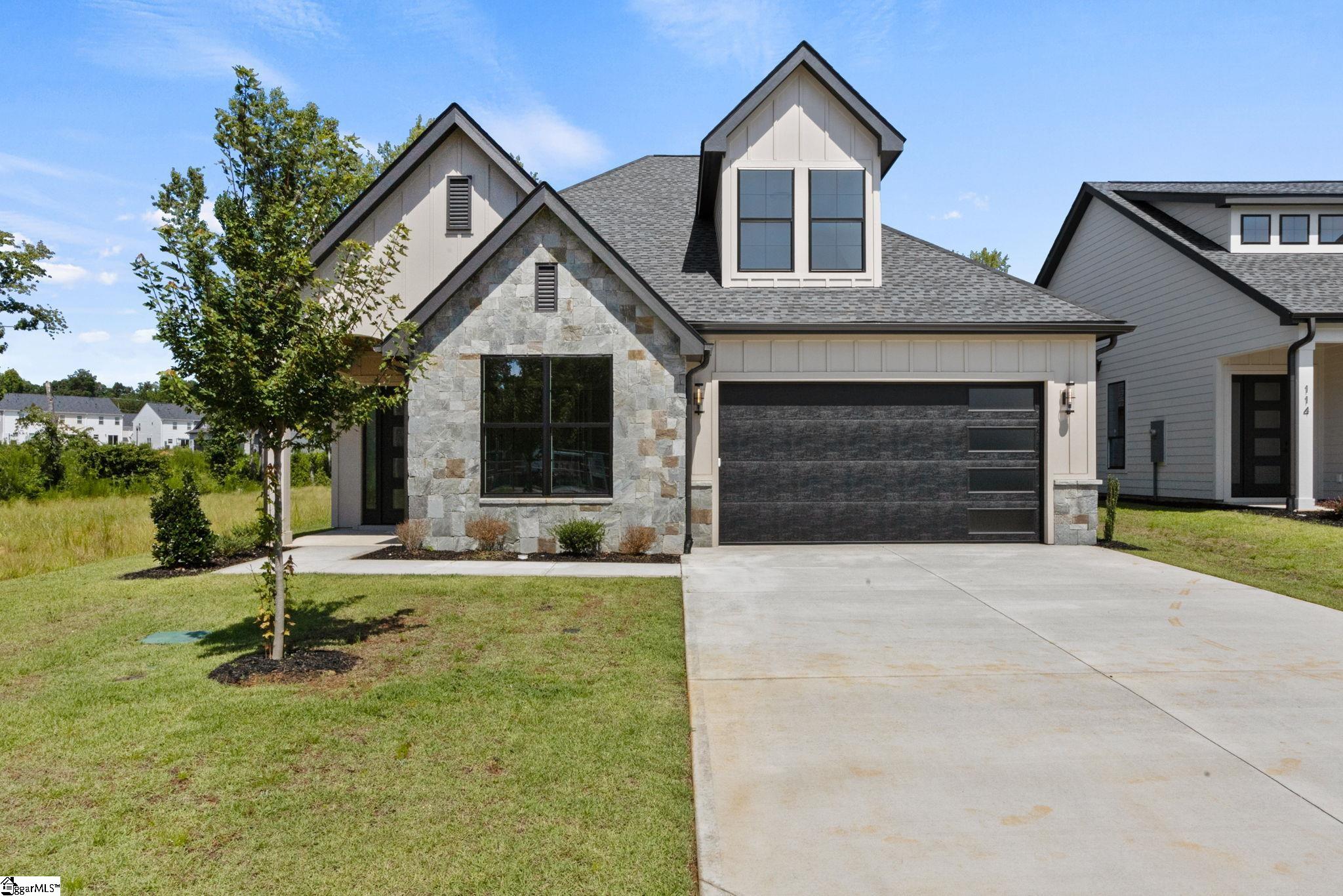 Modern home with a stone facade, dark garage door, and wide concrete driveway.