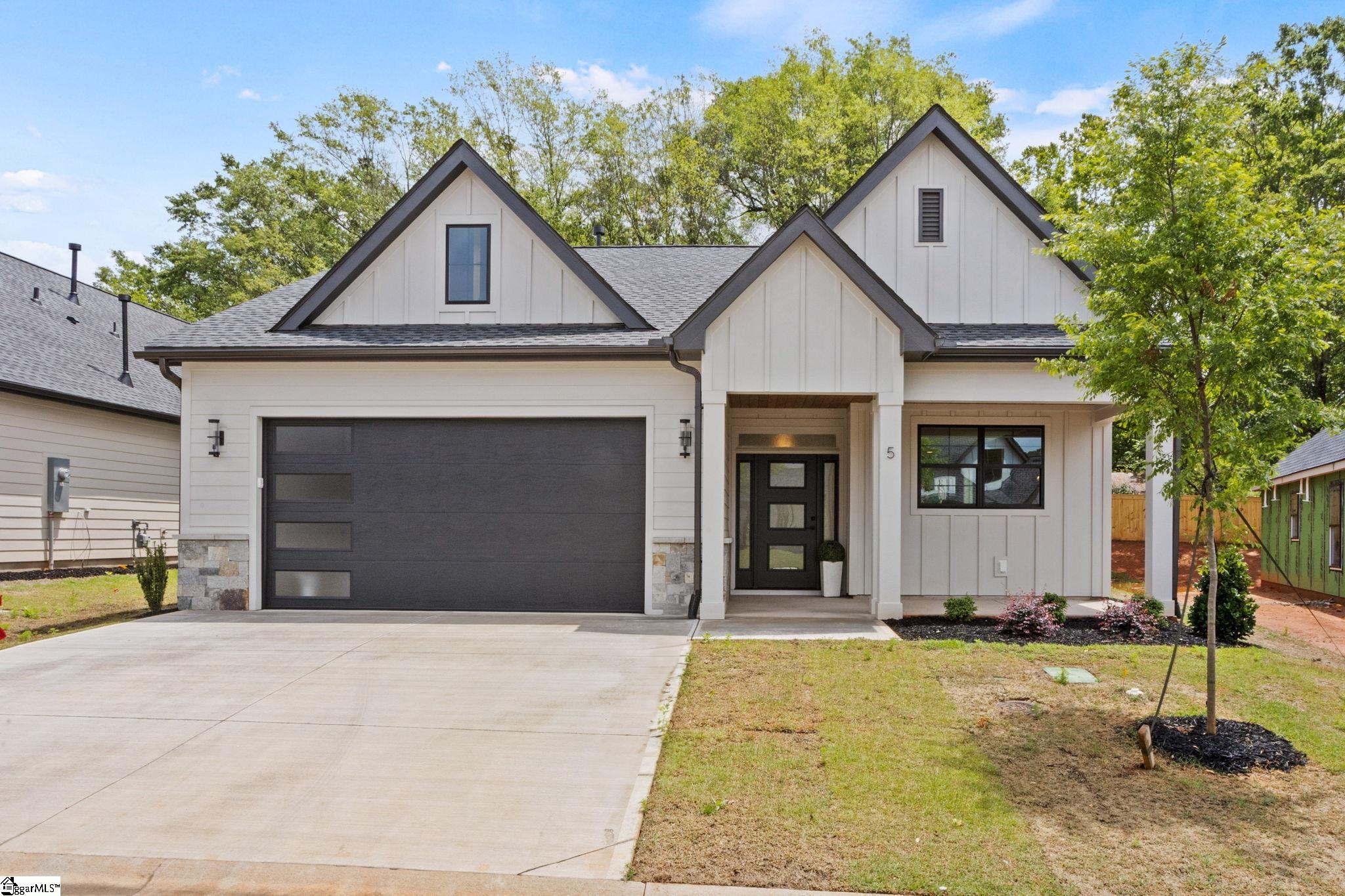 White modern farmhouse with multiple gables, a charcoal garage door, and a covered entry.