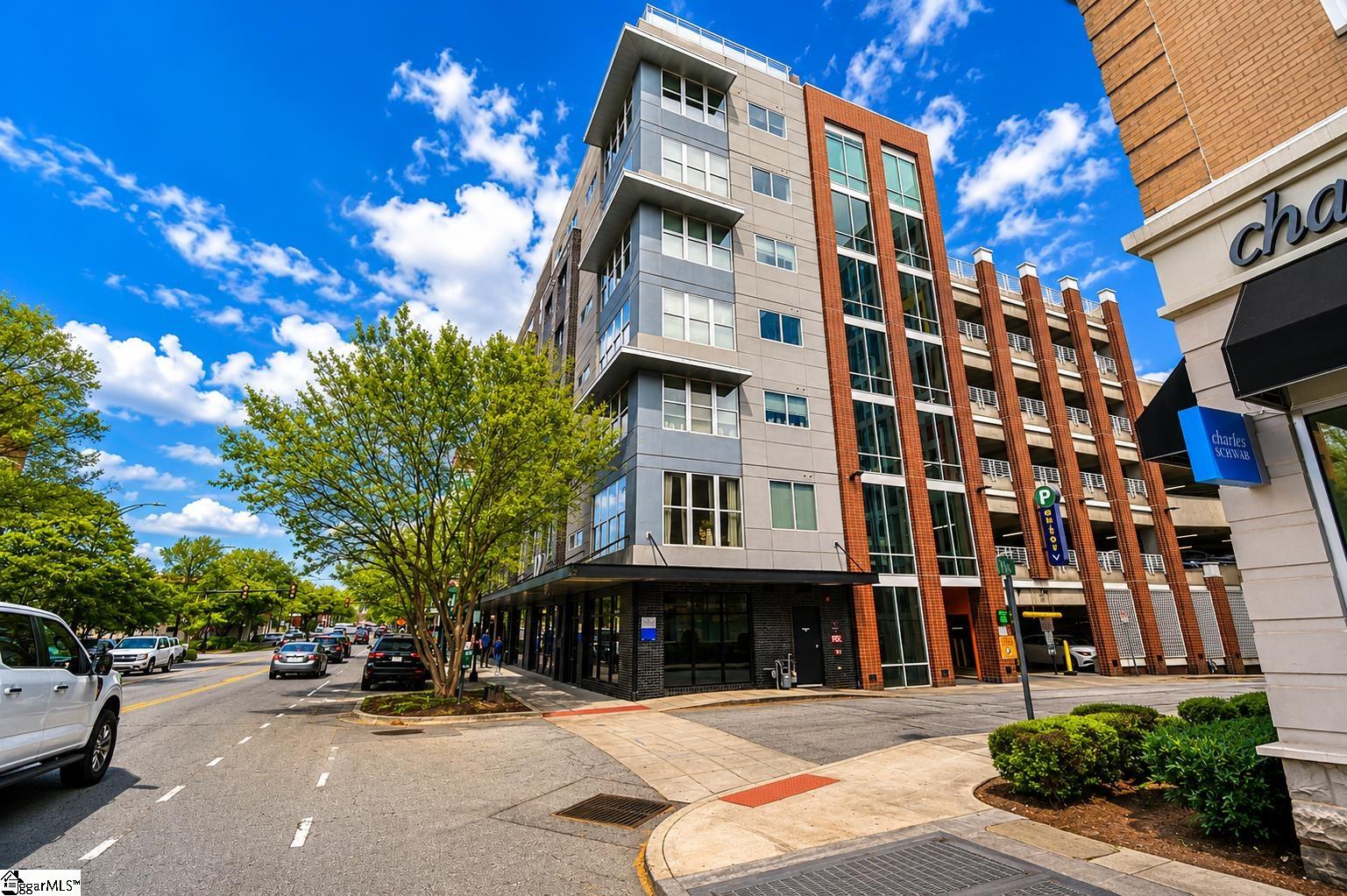 Modern gray-and-brick multi-story building with large windows beside a parking garage.
