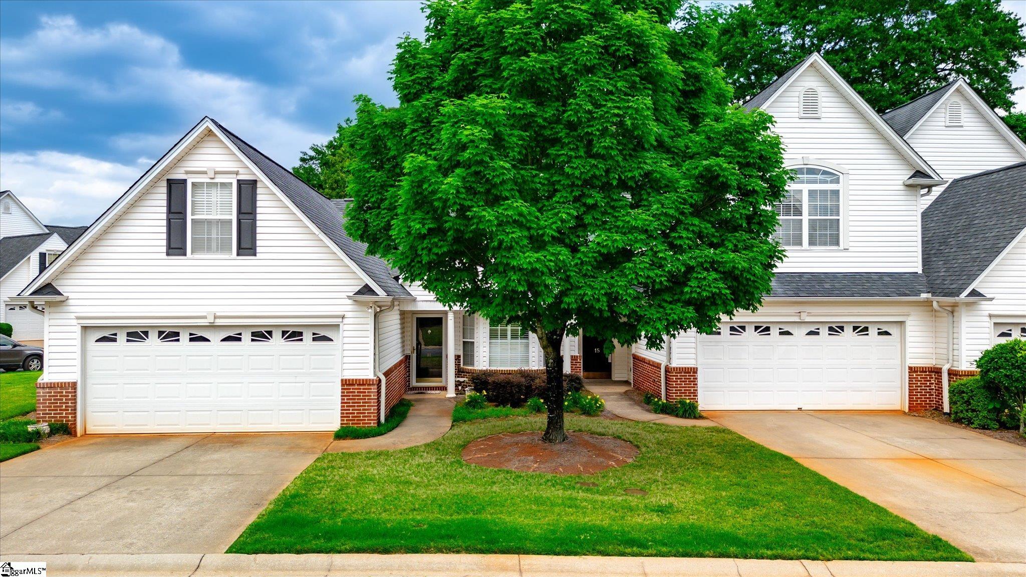White-sided home with brick accents, two garage doors, and a large leafy tree in front.