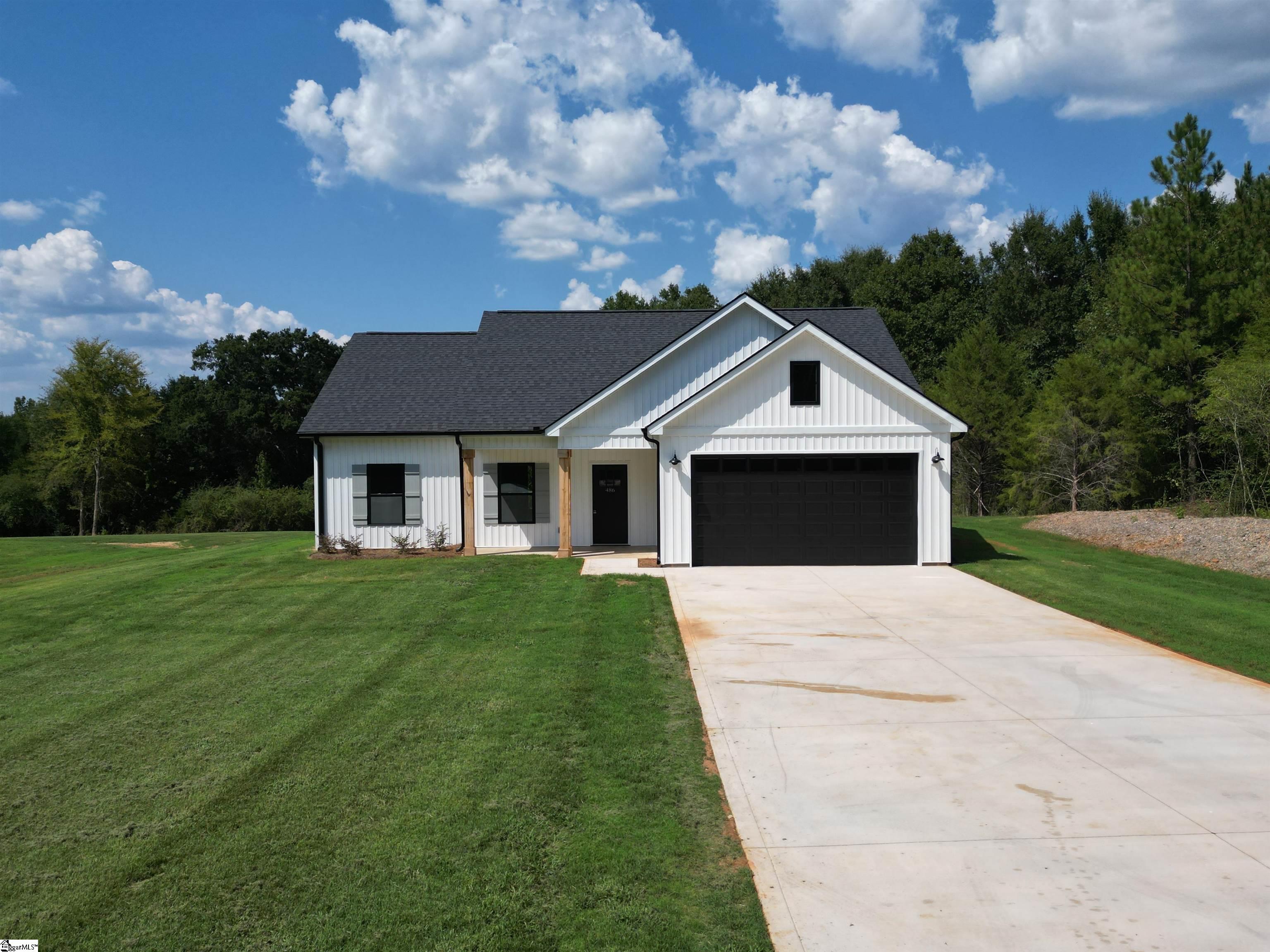 White-sided home with a black double garage door, broad driveway, and tree-lined lawn.