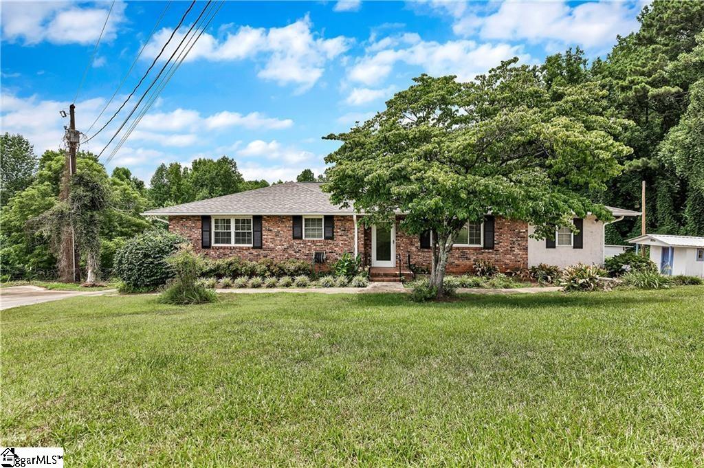 Single-story brick ranch house with black shutters, a broad lawn, and a large shade tree.