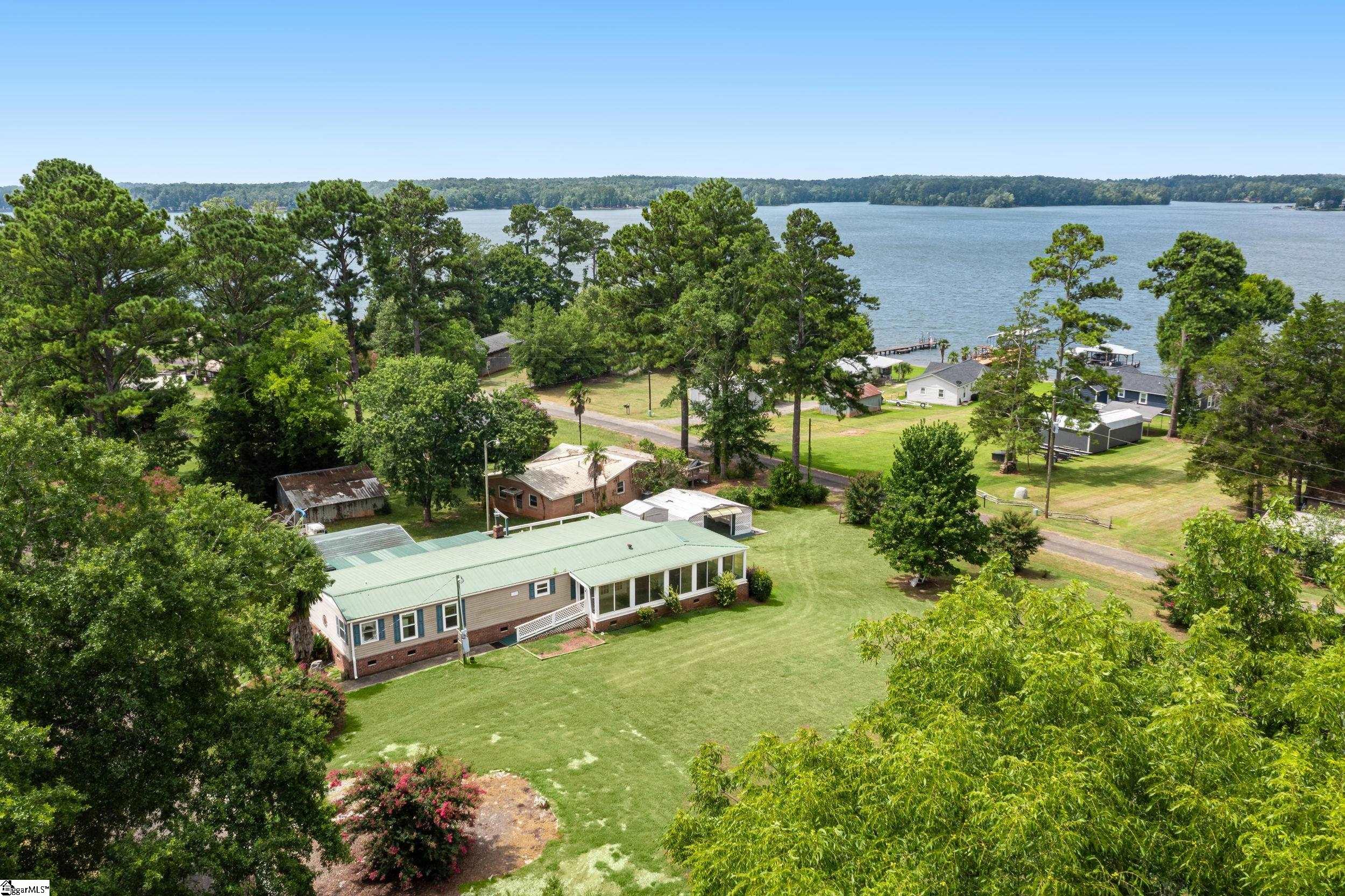 Single-story lakeside home with a pale green roof, broad lawn, and wooded shoreline.