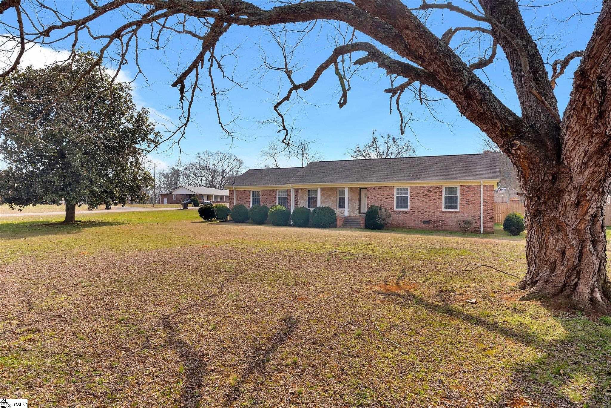 Single-story brick house behind a broad lawn, framed by a large mature tree.