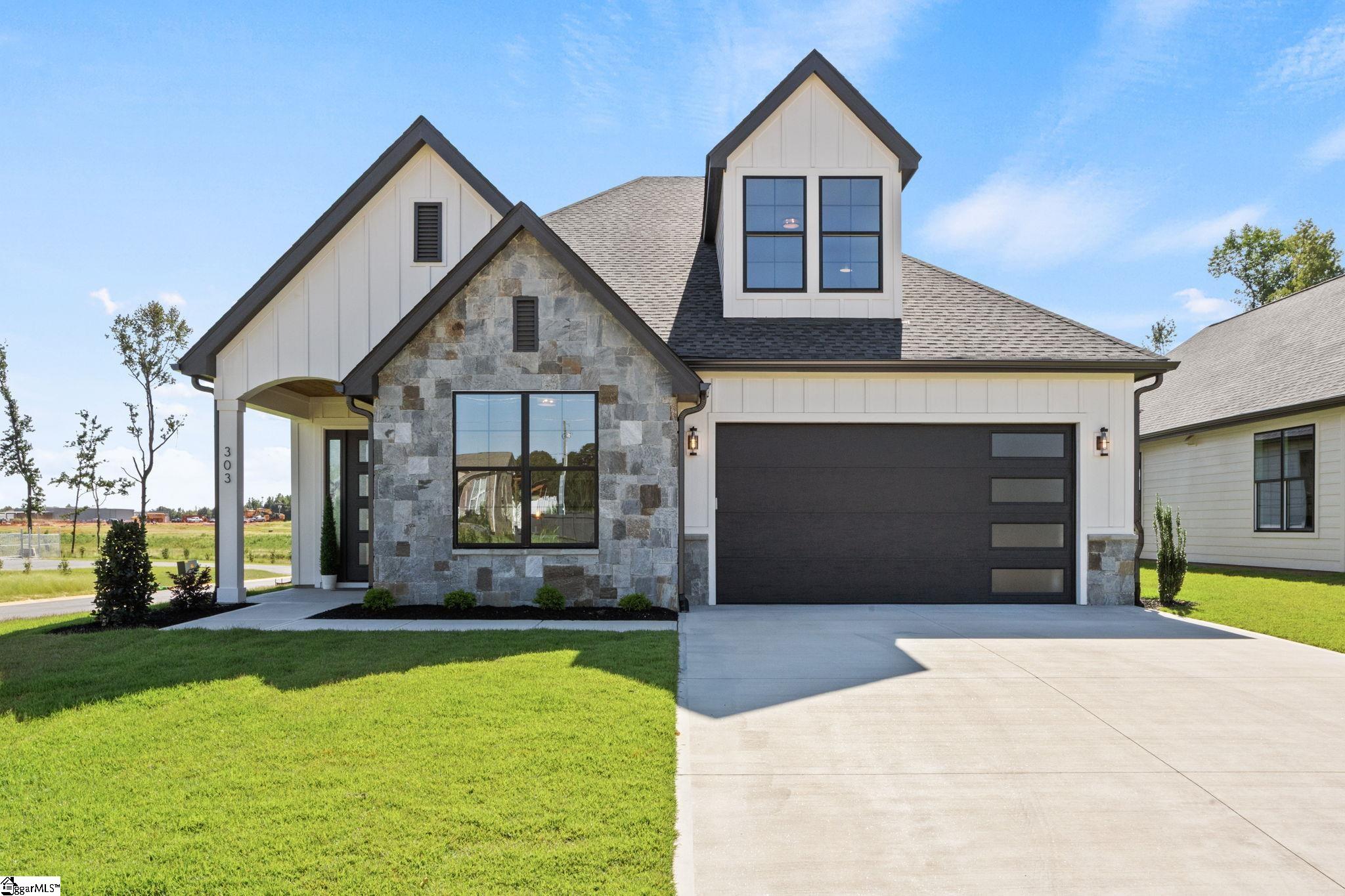 Modern two-story house with gray stone facade, steep gables, and a wide driveway.