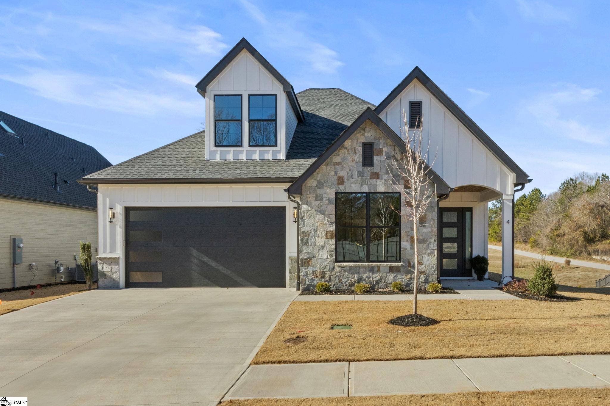 Two-story house with a stone facade, dark two-car garage, and leafless tree in the front lawn.