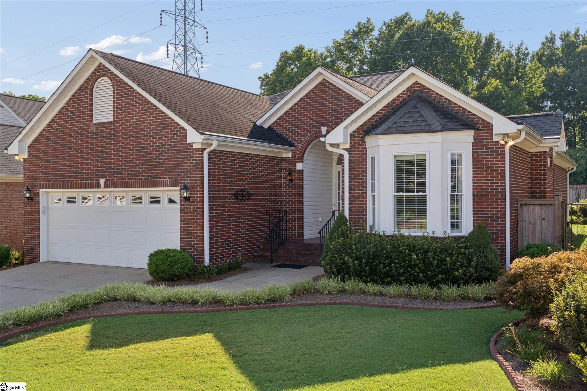 Red-brick house with white trim, a two-car garage, bay window, and landscaped front lawn.