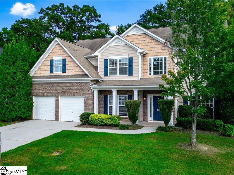 Two-story house with tan shingles, brick lower level, blue shutters, and an attached two-car garage.
