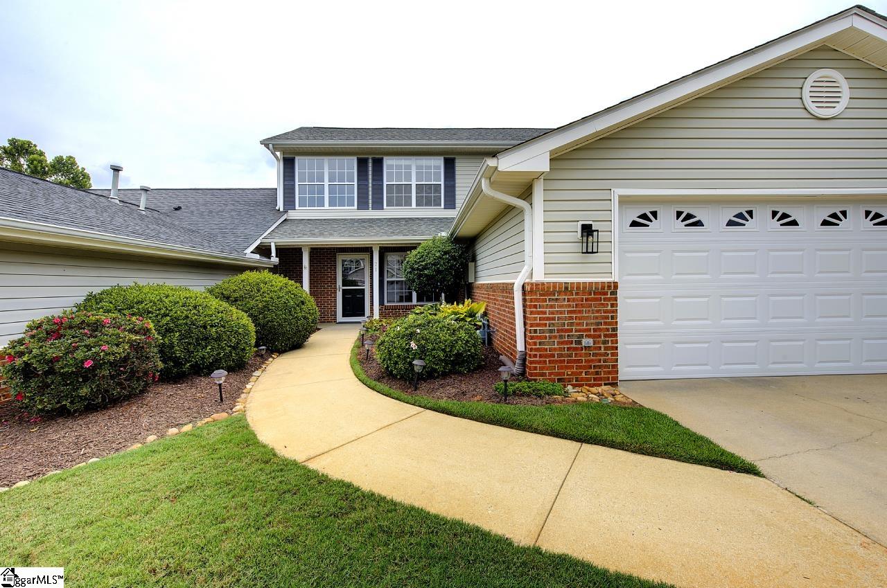 Two-story home with brick accents, a double garage, and a curved walkway through landscaped shrubs.