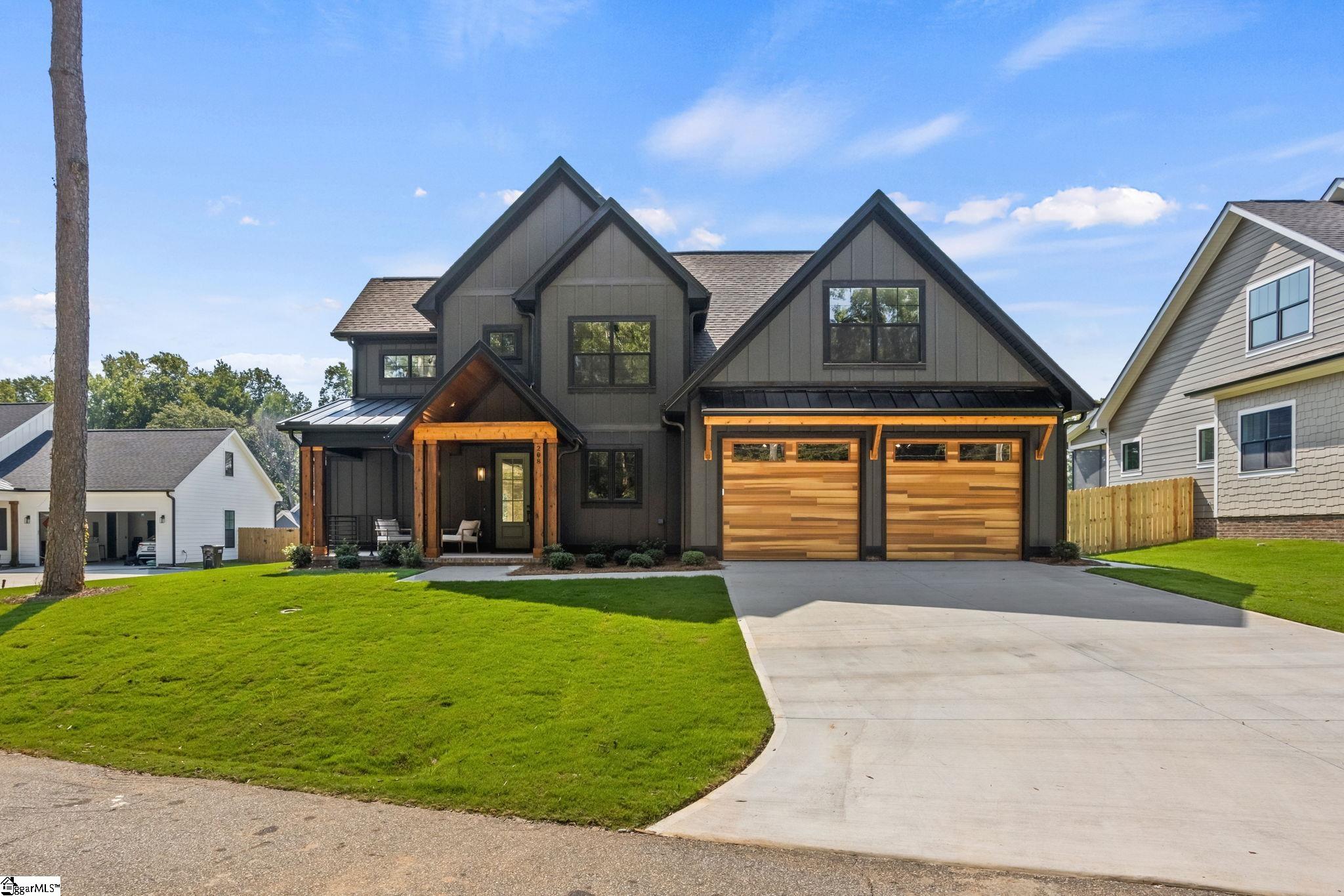 Dark-gray gabled home with twin wood garage doors, a covered porch, and a broad concrete driveway.