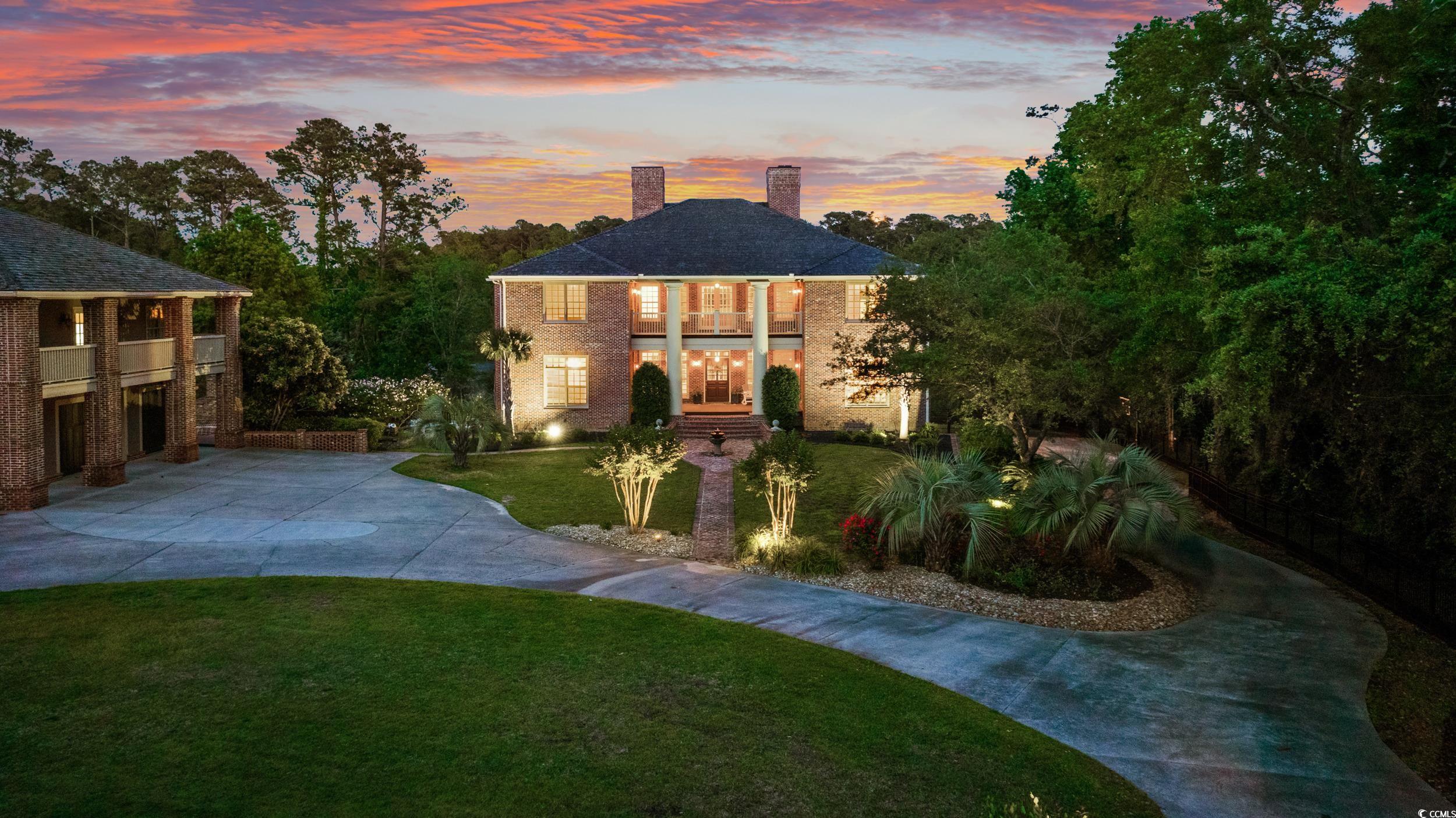 Two-story brick home at dusk with a columned porch and curved driveway.