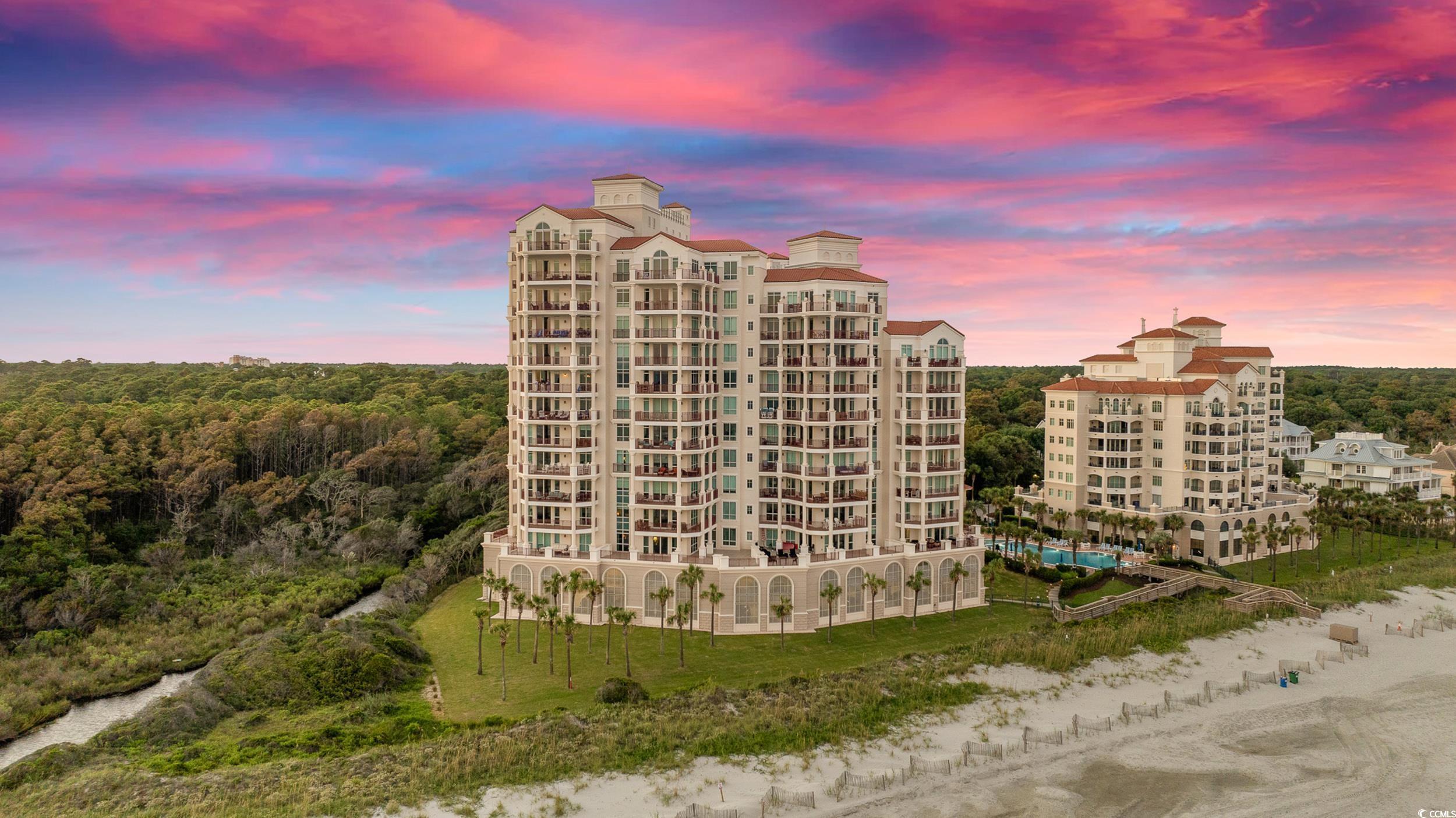 Beachfront condominium towers with balconies and a pool beneath a vivid pink dusk sky.
