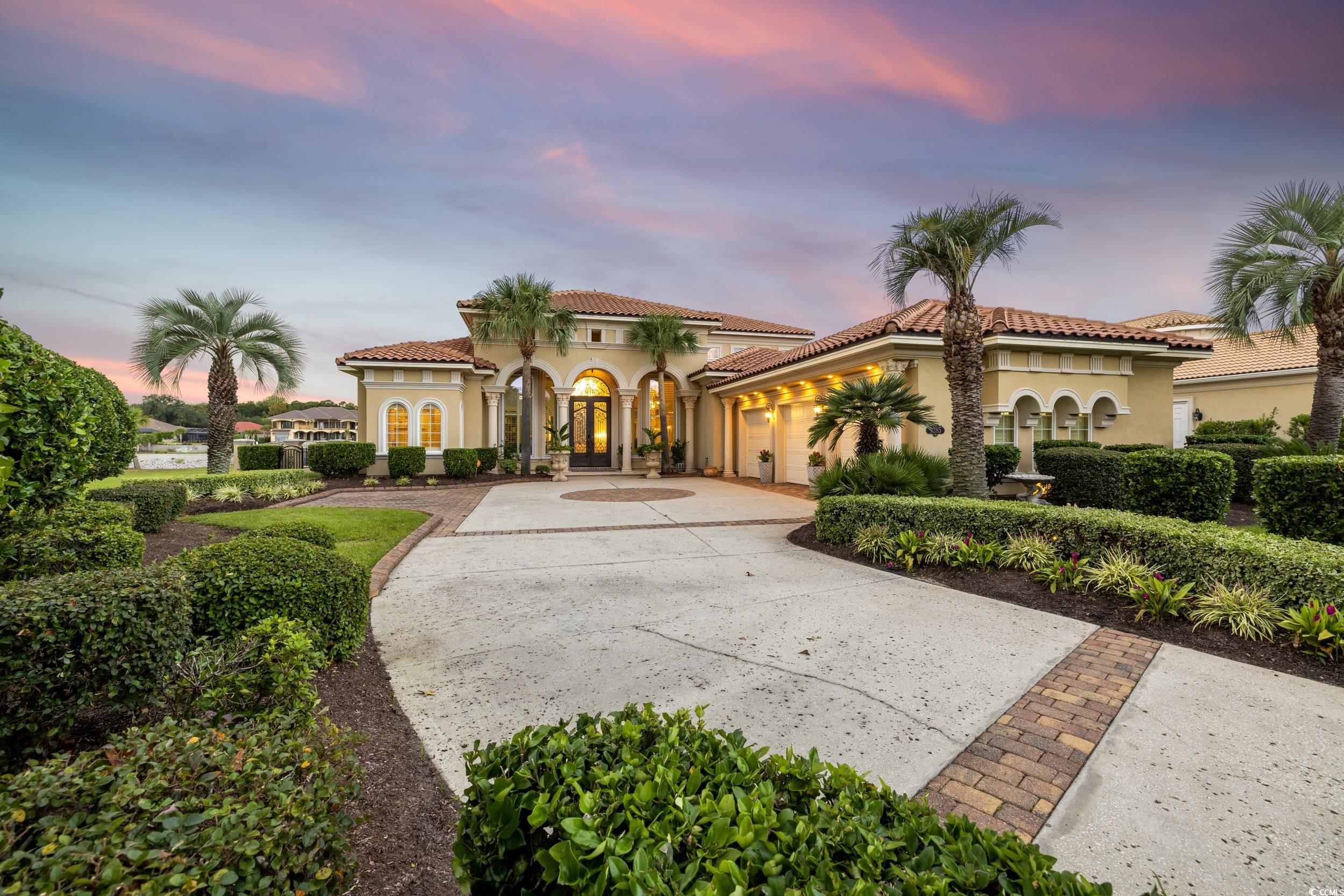 Mediterranean-style home with arched entry, palm trees, and a broad curved driveway at dusk.