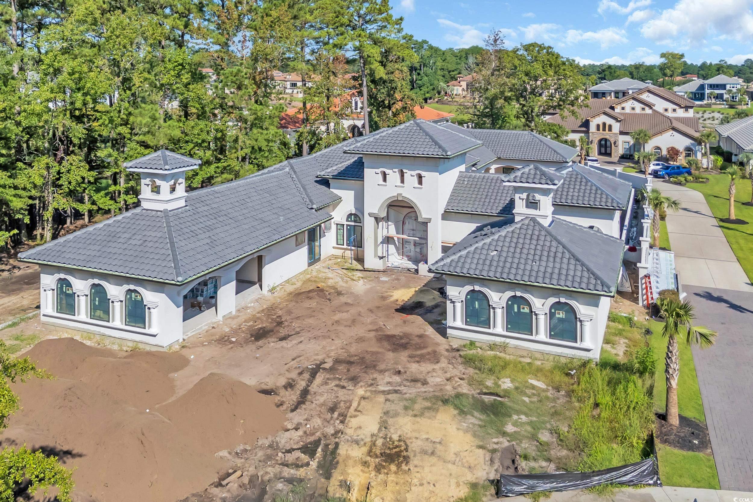 Large white stucco house under construction with gray tile roofs and arched windows, seen from above.