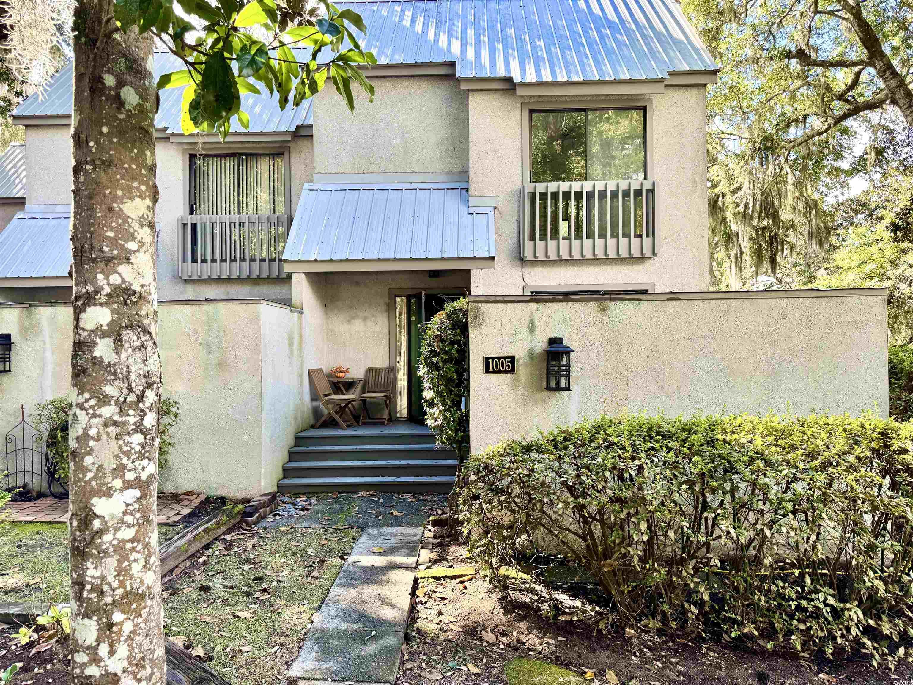 Two-story stucco home with blue-gray metal roofs, a leafy front yard, and entrance marked 1005.
