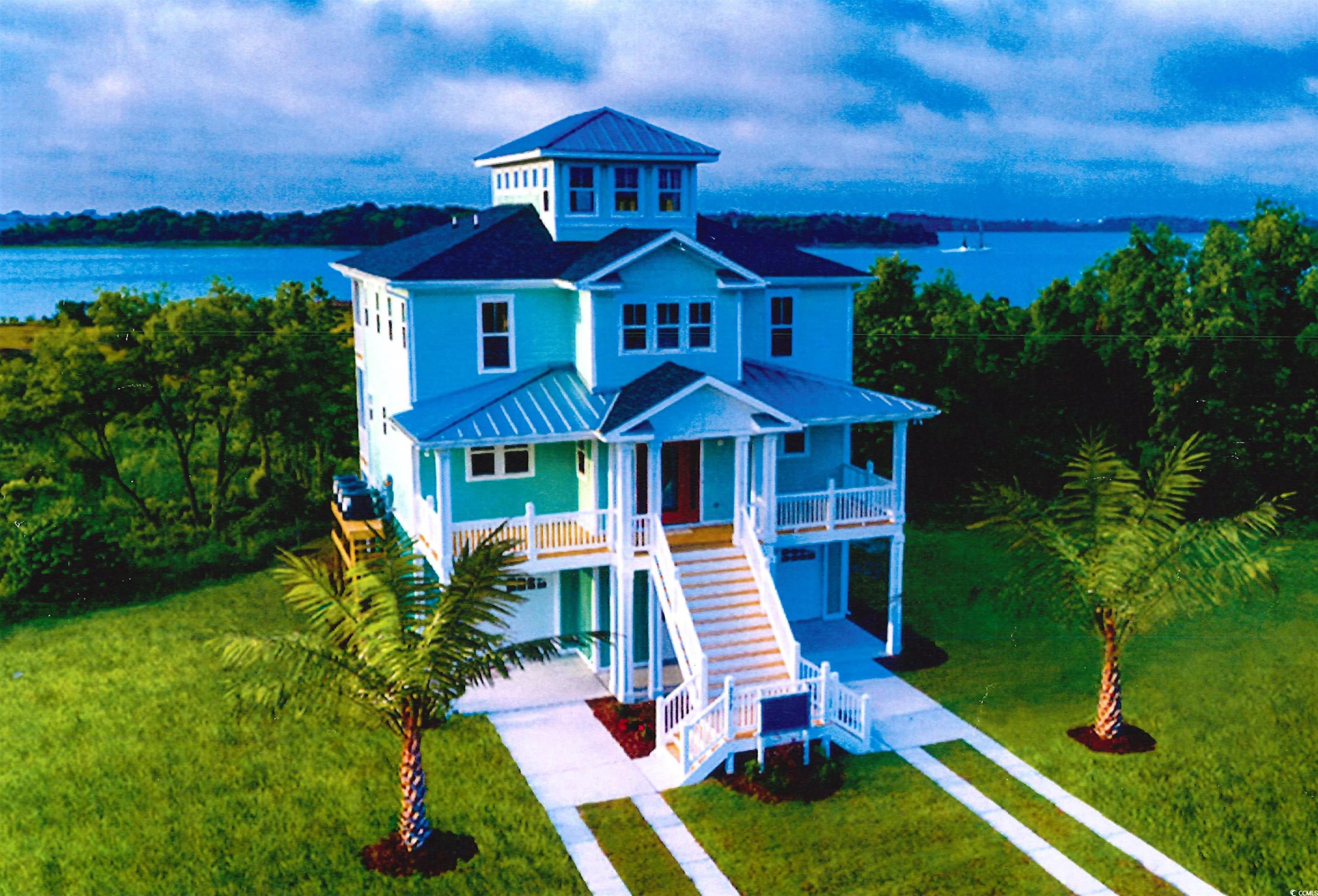 Multi-story blue coastal house with white porches and a bay view behind it.