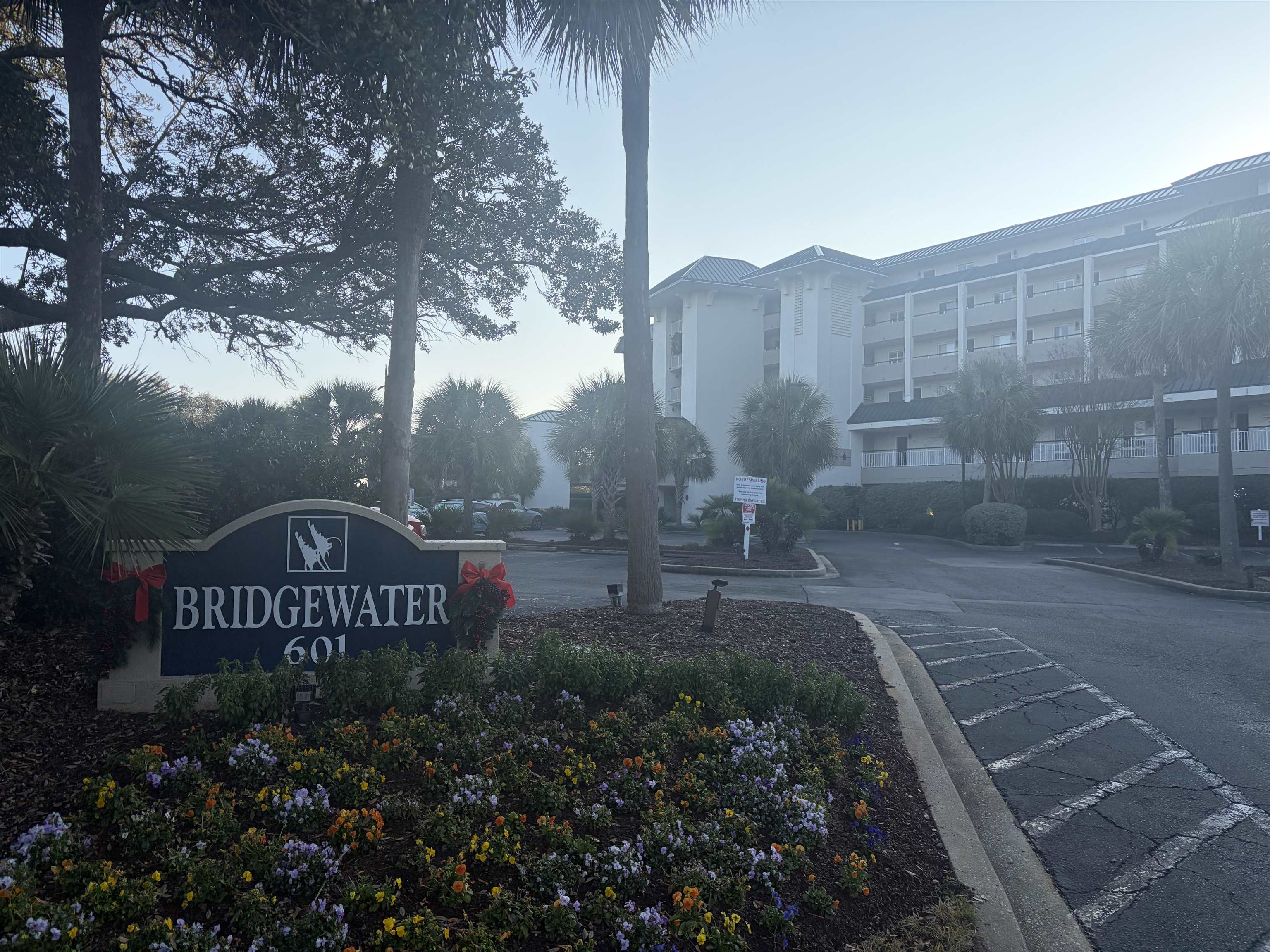 Bridgewater condominium exterior and entrance sign, surrounded by palm trees and flower beds.