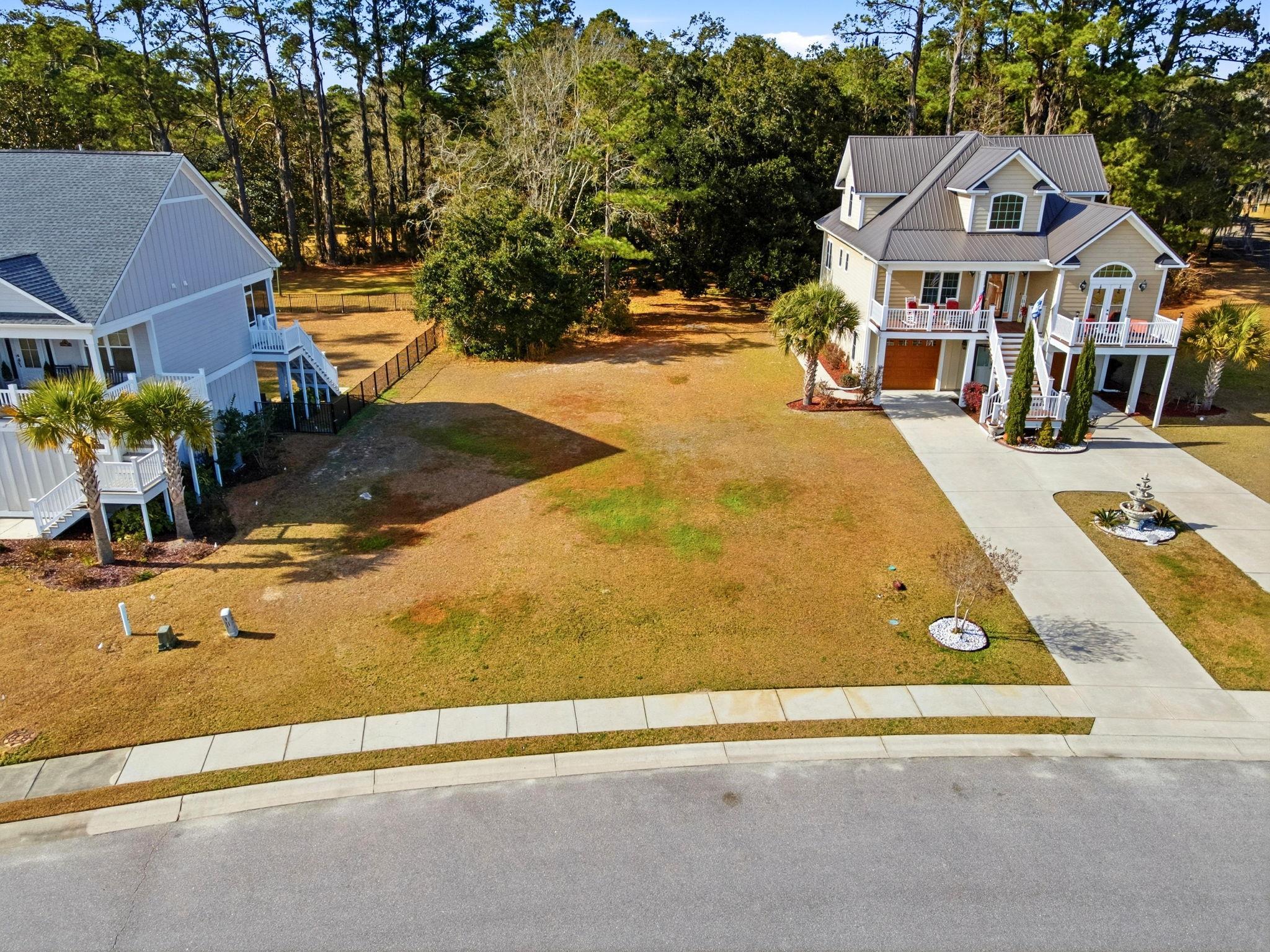 Vacant residential lot between two homes, with a grassy yard and mature trees along the rear boundary.