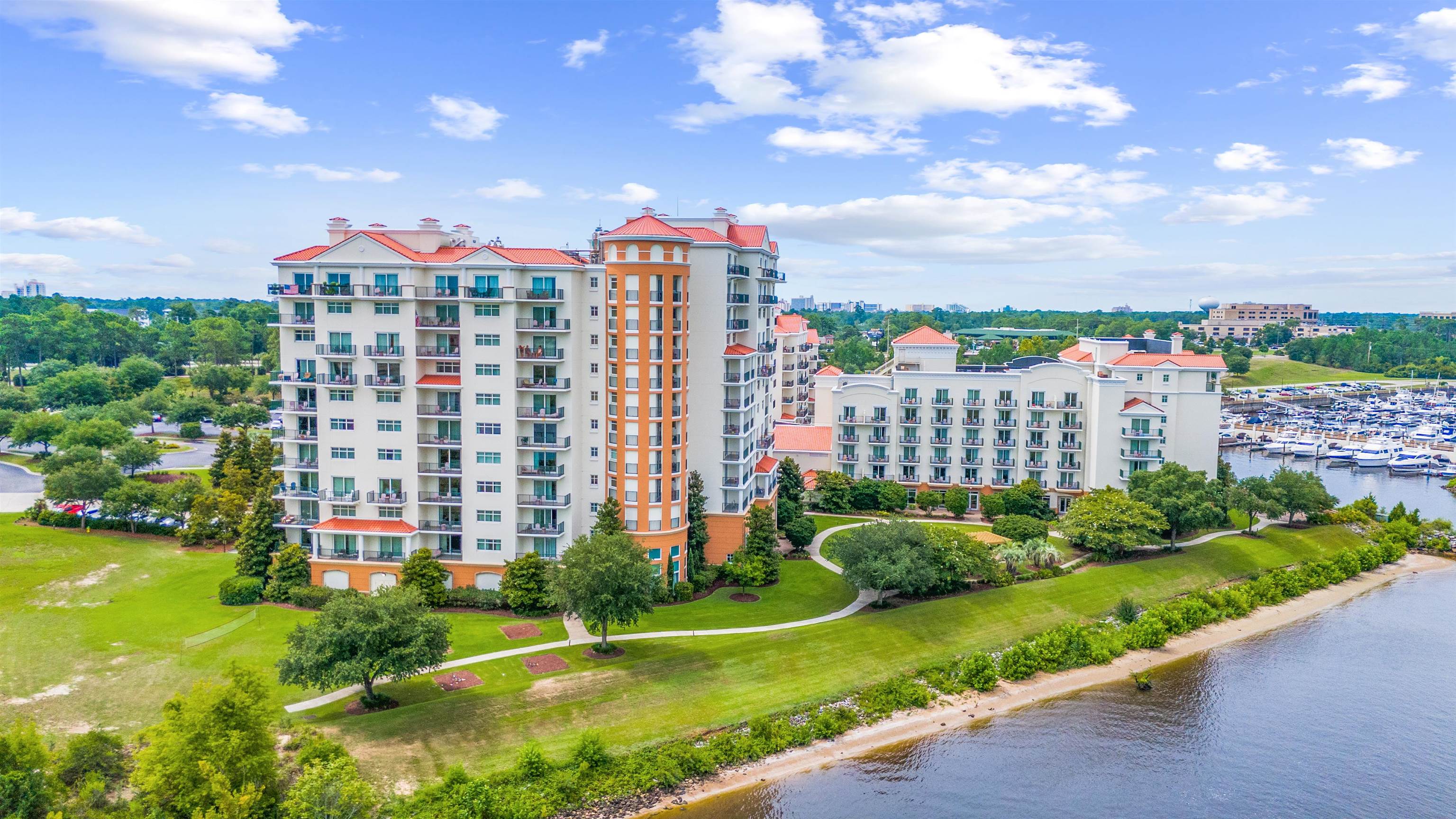 Waterfront condominium complex with red tile roofs, landscaped grounds, and marina boats.
