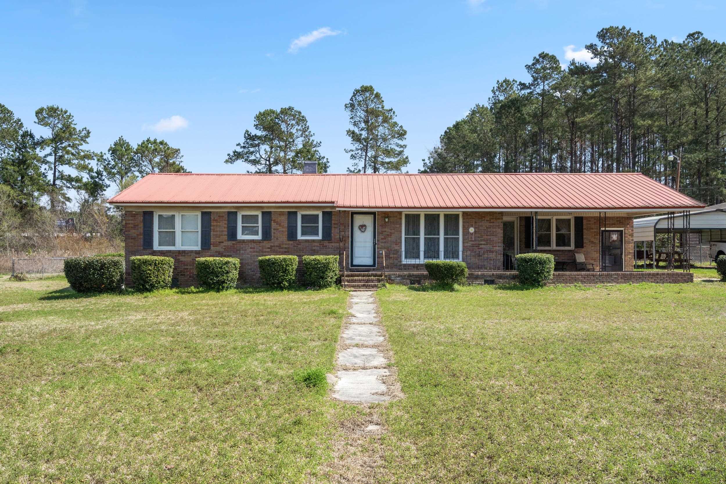 Single-story brick house with a red metal roof, blue shutters, and a walkway through the front lawn.