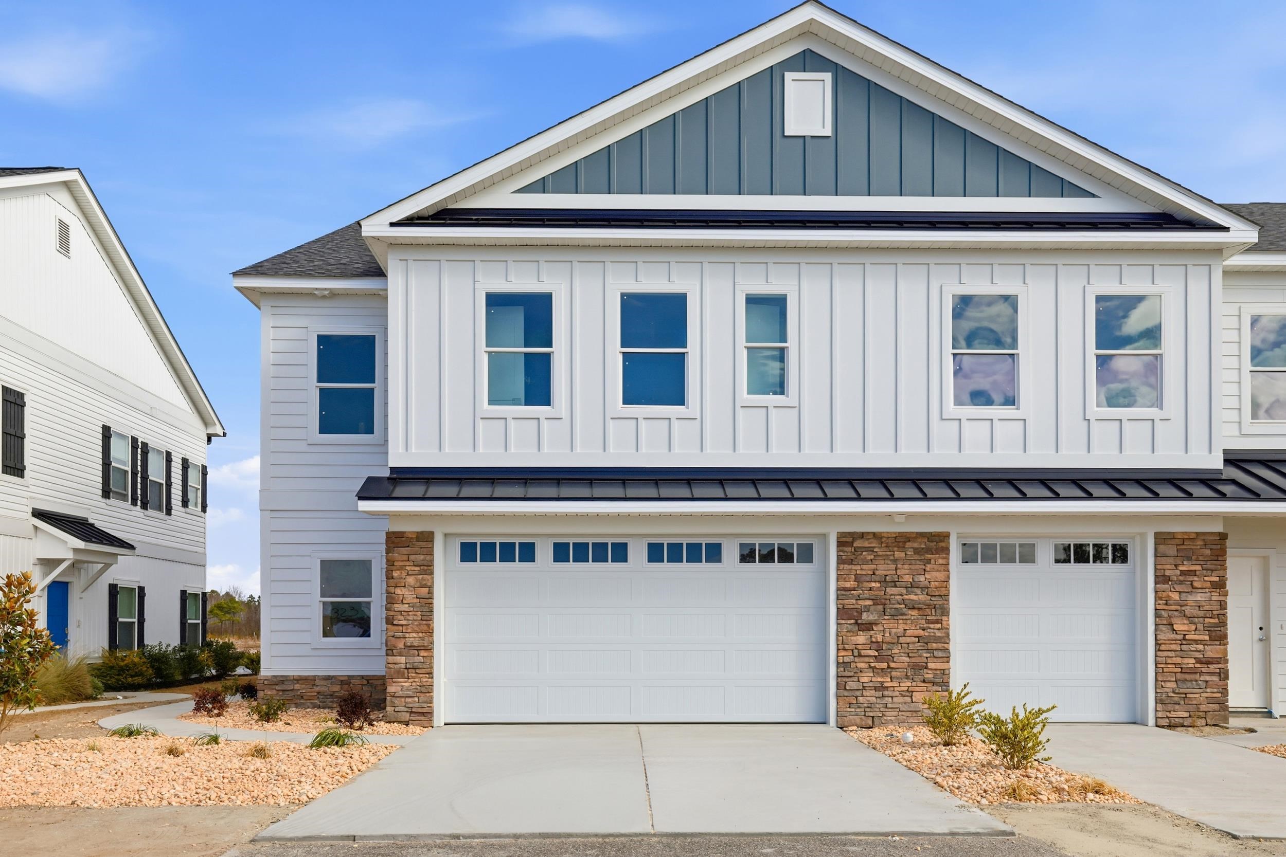 Two-story home with a blue gable, stone accents, and two garage doors.