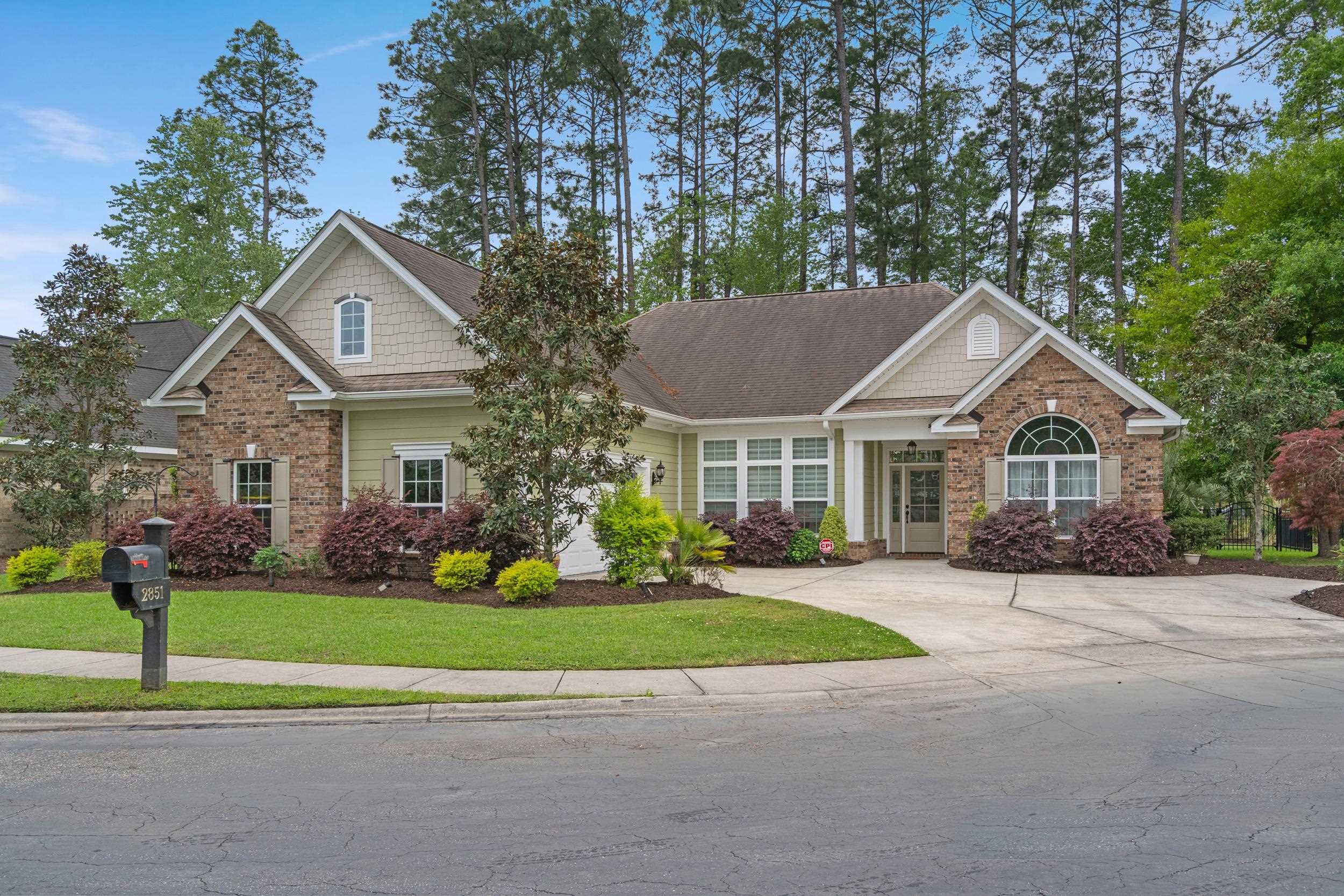 Brick and pale green house with an arched front window, landscaped shrubs, and mailbox marked 2851.