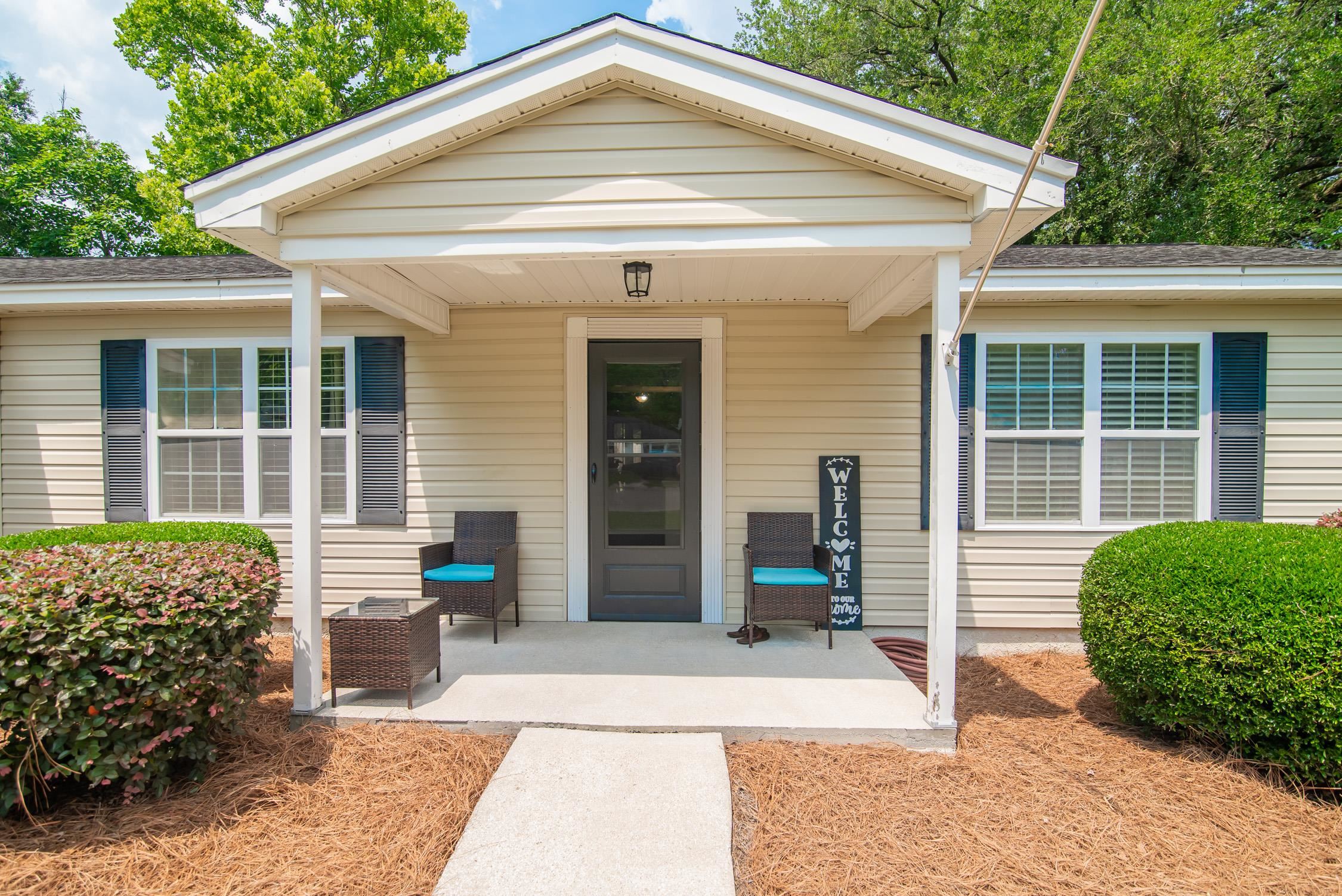 Single-story cream home with a covered porch, wicker chairs, turquoise cushions, and a welcome sign.