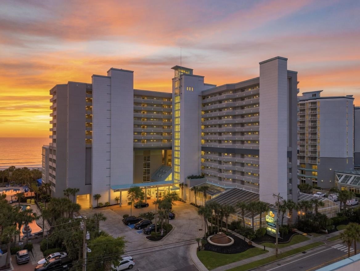 Oceanfront condominium with rows of balconies and the ocean visible at sunset.