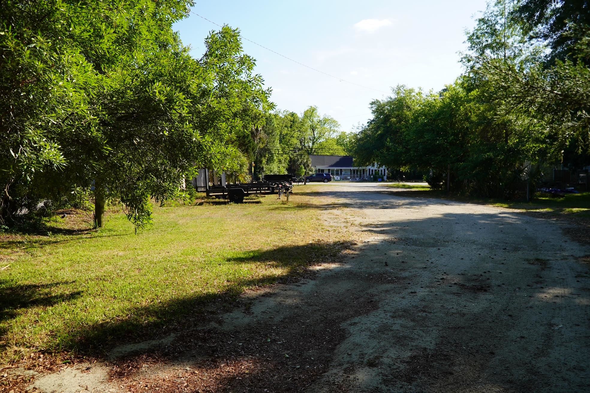 Tree-lined gravel driveway leading to a low building, with a trailer parked beside it.