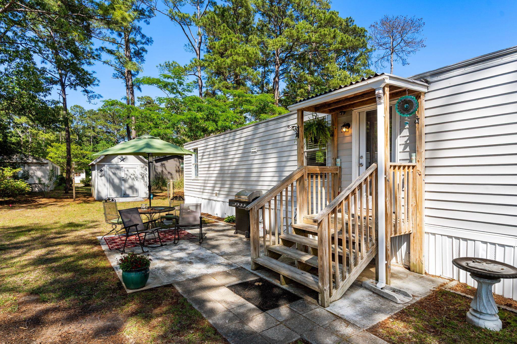 White-sided home with a covered wooden porch, paved patio, outdoor seating, grill, and backyard shed.
