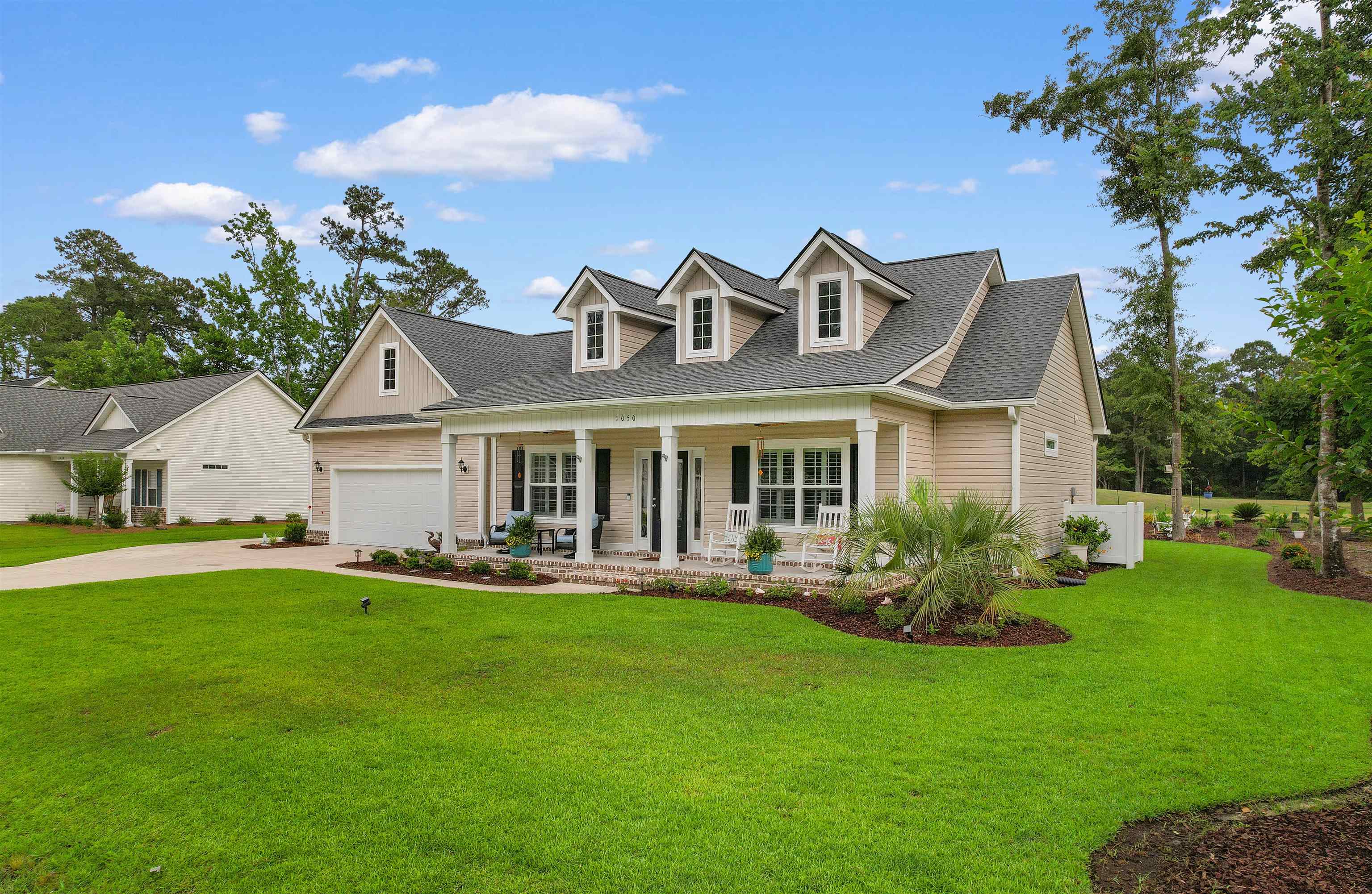 Beige house with three dormers, a covered porch, and a wide green lawn.