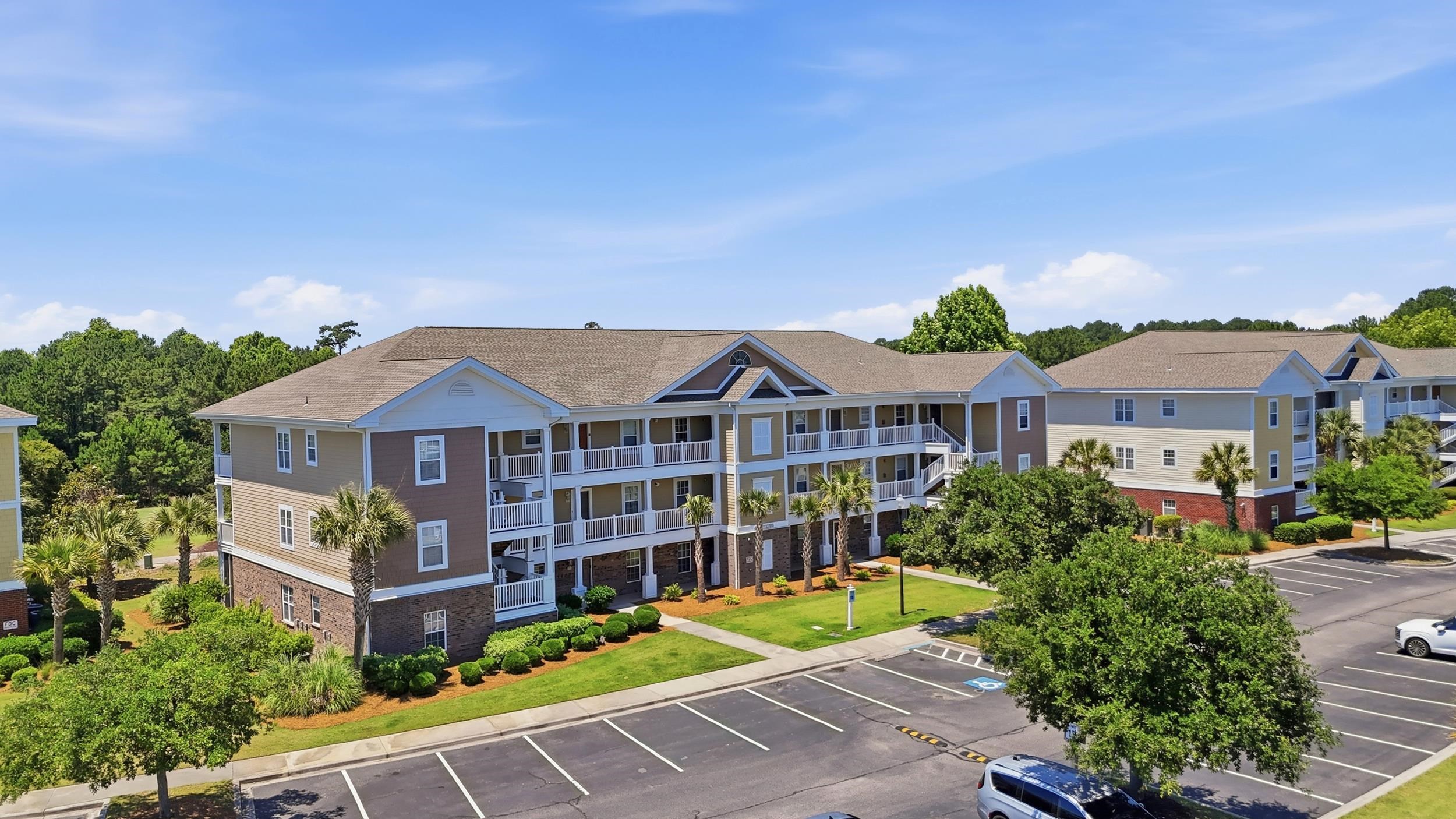 Condominium buildings with covered balconies, palm trees, landscaped grounds, and a parking lot.