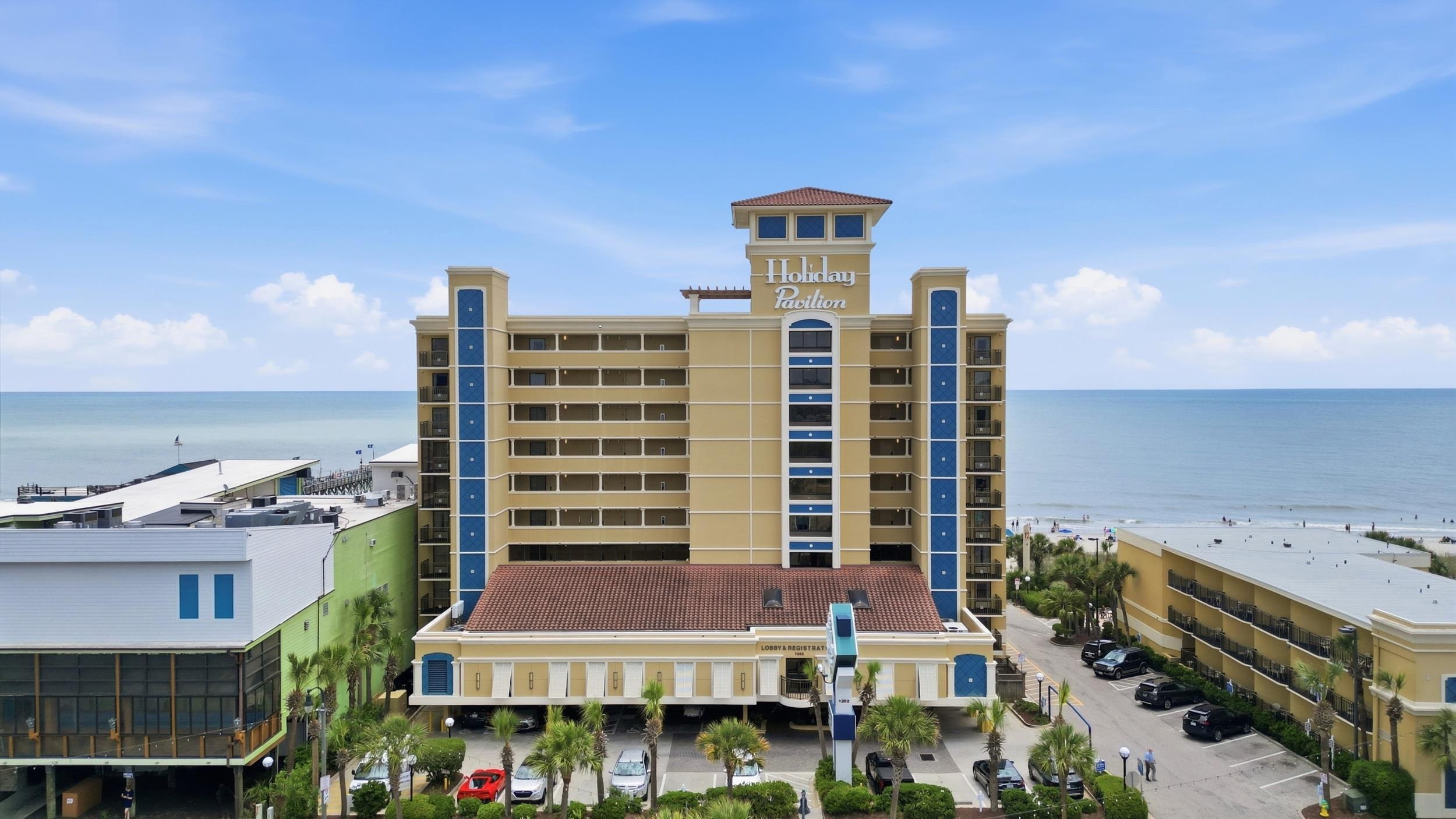 Holiday Pavilion beachfront condominium beside the ocean, with balconies and palm trees.