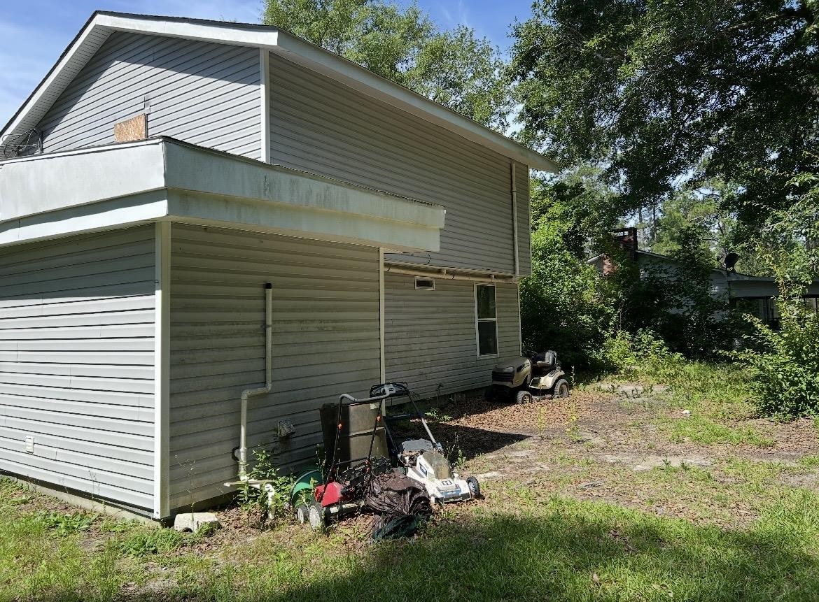 Gray-sided house with a covered carport and lawn equipment in the yard.