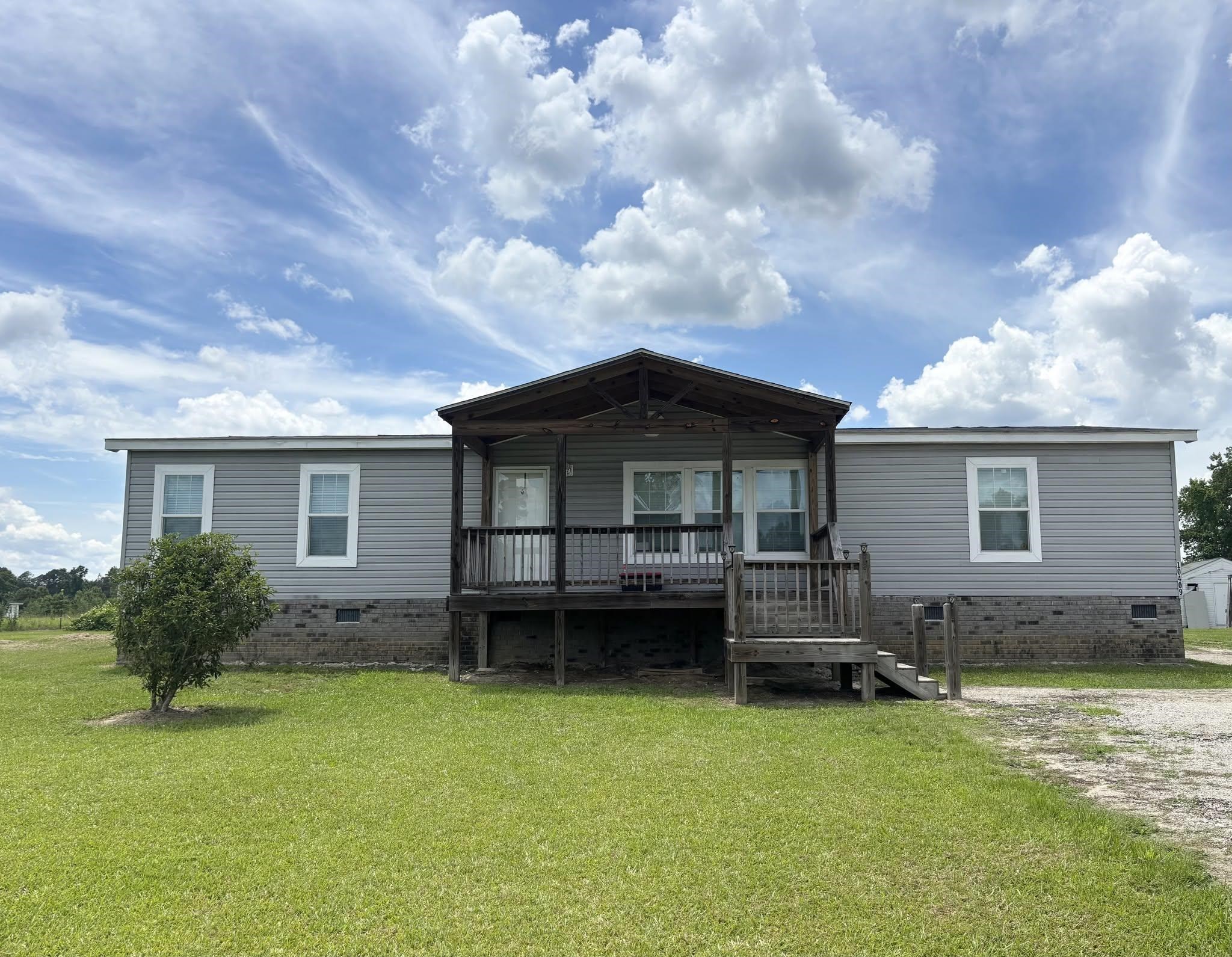 Gray single-story home with a raised covered porch and broad green lawn.