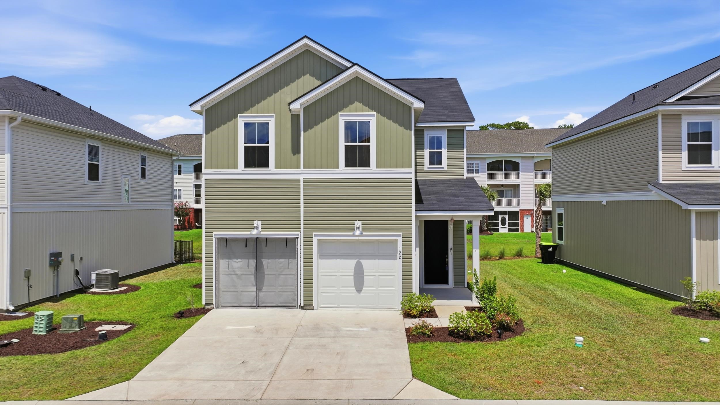 Two-story green townhouse with white trim, garage doors, driveway, and lawn.
