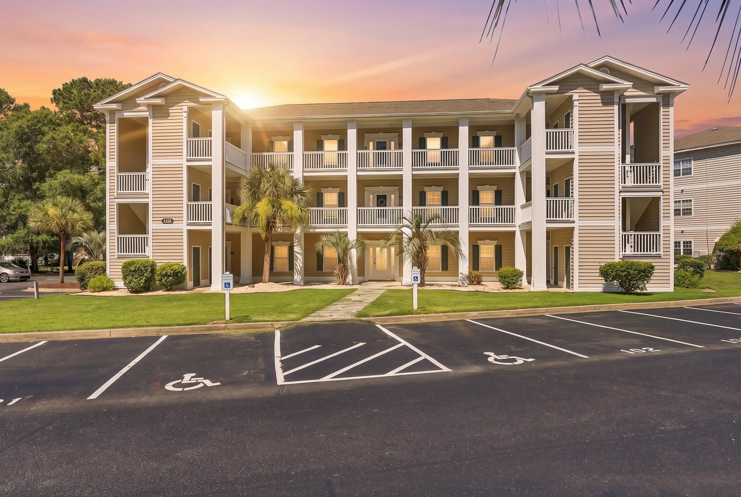 Three-story apartment building with white balconies and accessible parking spaces at sunset.