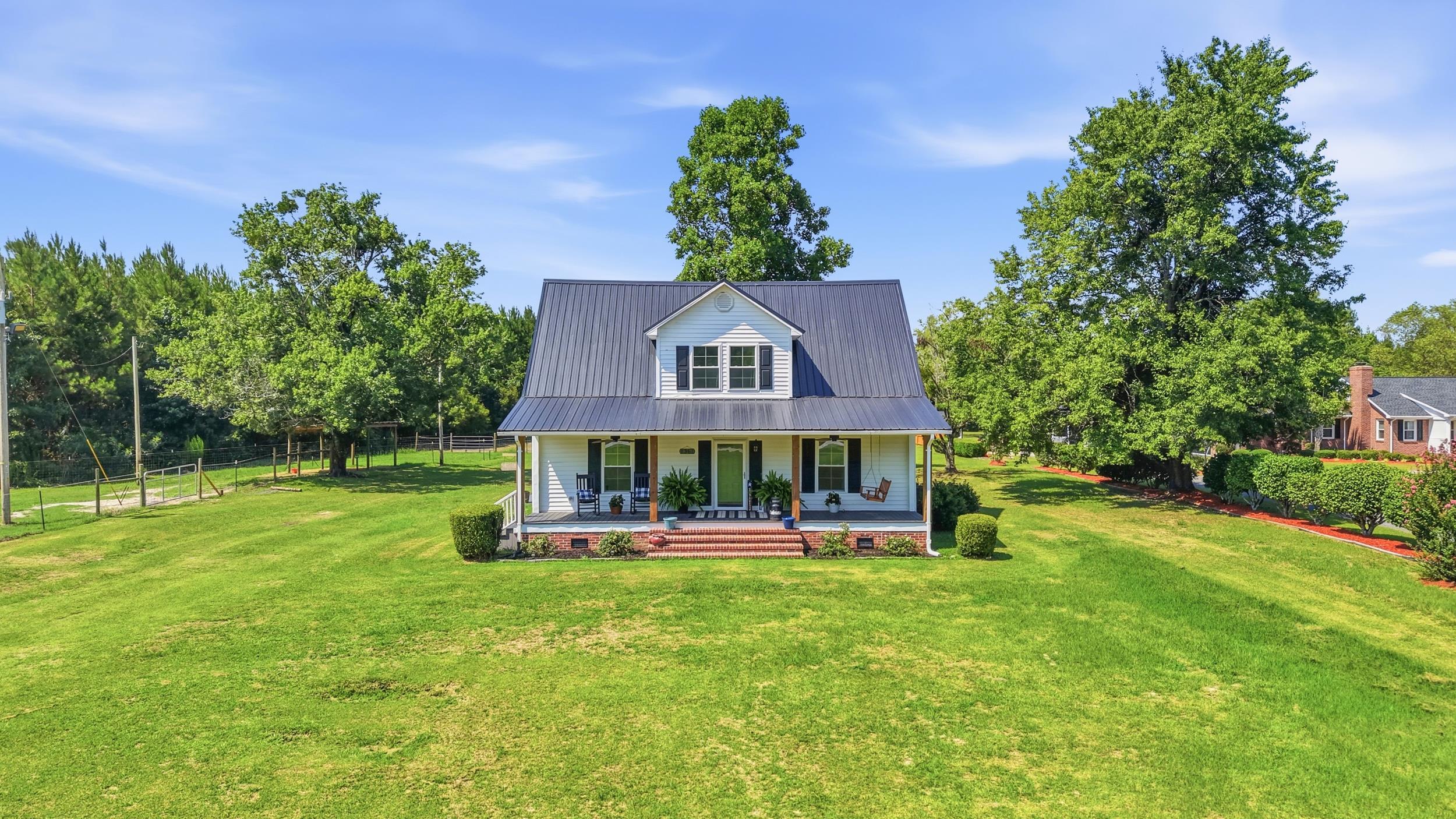 White two-story house with a dark metal roof, covered porch, and broad green lawn.