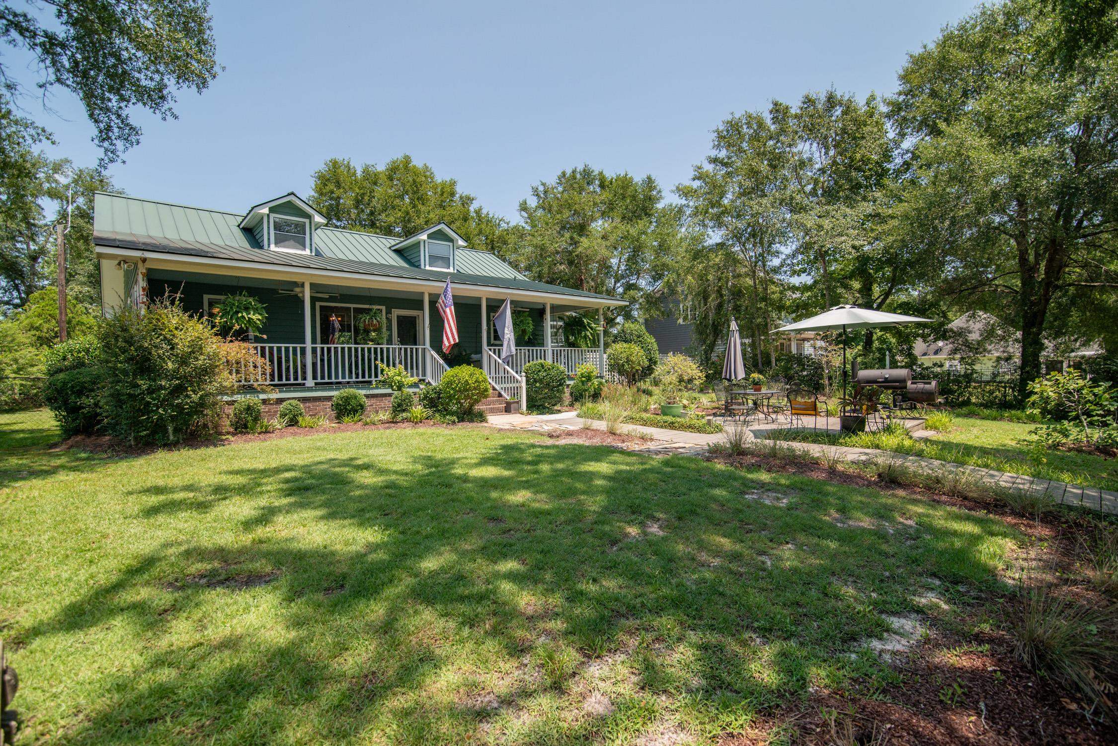 Green house with a covered porch and metal roof beside a landscaped lawn and patio.