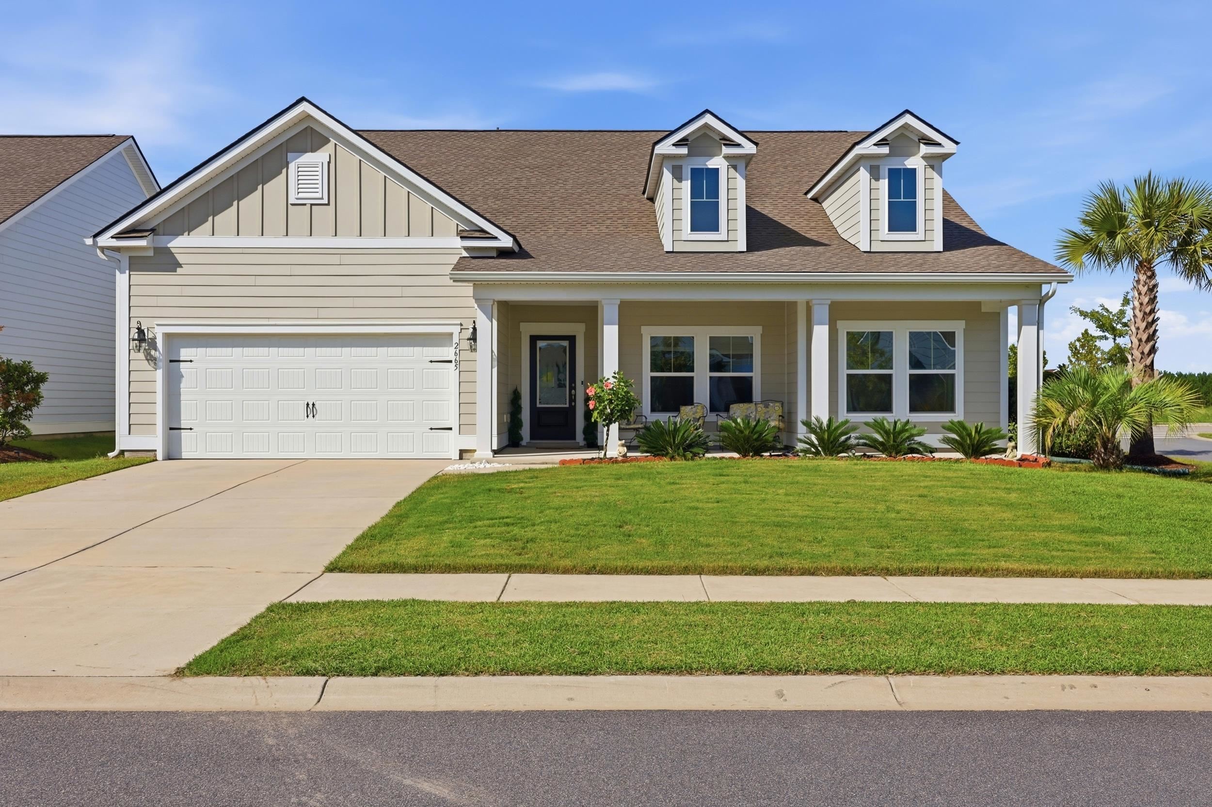 Two-story beige house with a double garage, covered porch, dormers, and palm trees.